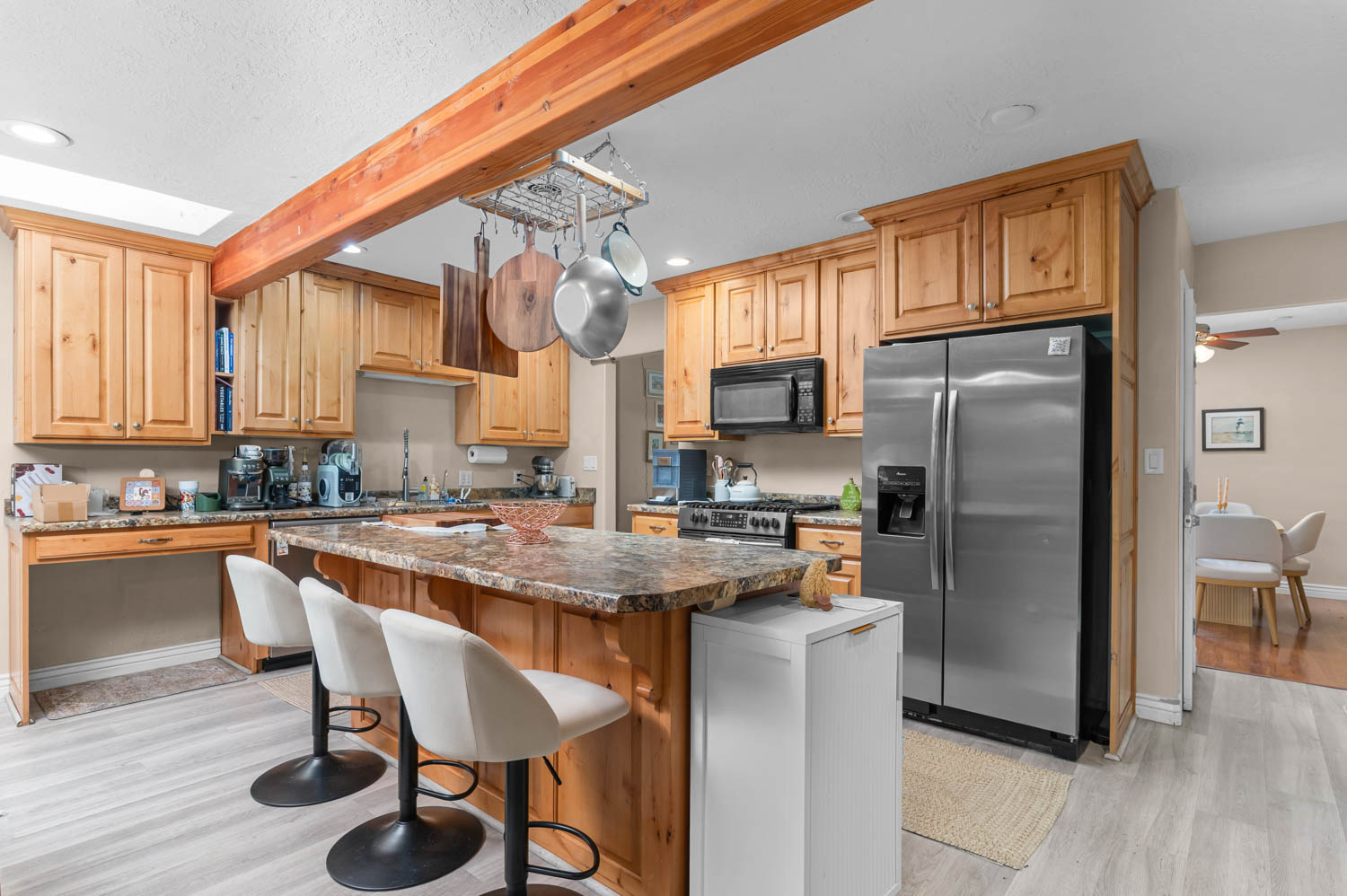 Kitchen featuring a central island with bar seating, wood-finish cabinetry, granite-style countertops, stainless steel appliances, and light wood-finish flooring