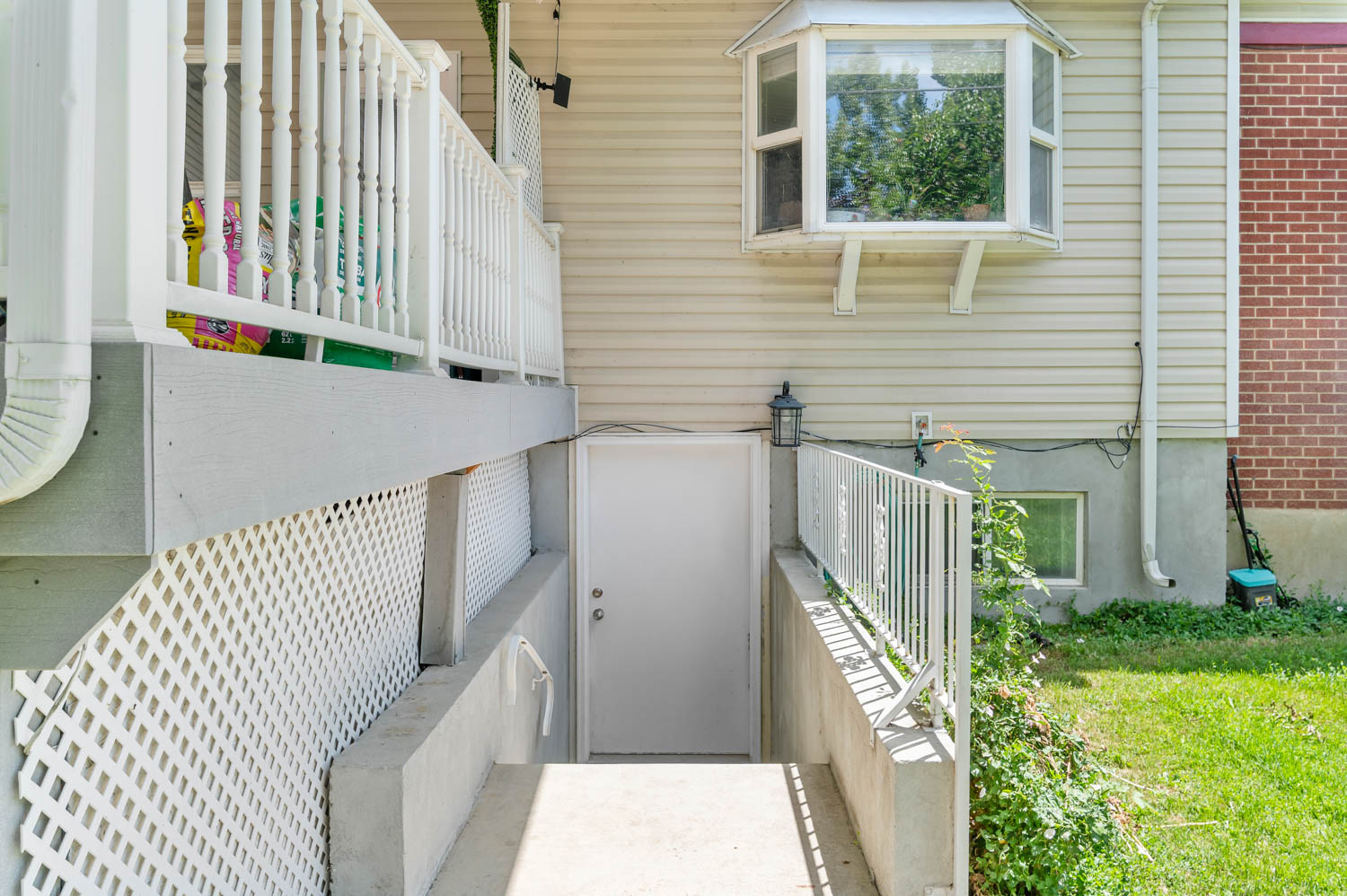Concrete pathway leading to a white door, featuring a white metal handrail and privacy lattice