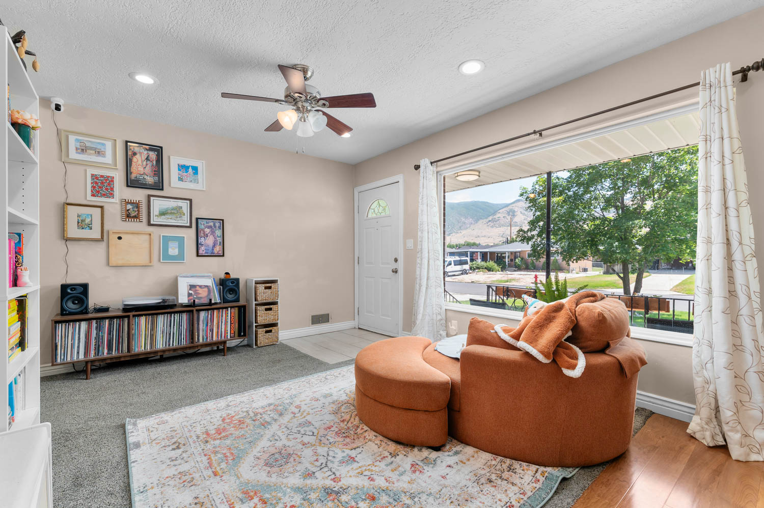 Living area featuring a large picture window, ceiling fan with integrated lighting, recessed lighting, and mixed flooring with carpet and wood-finish sections