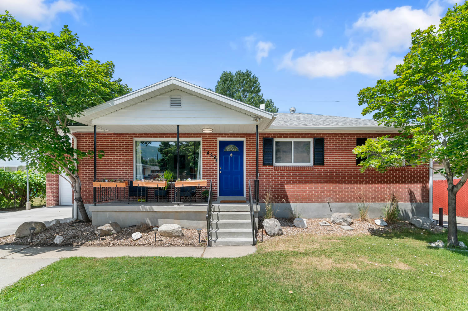 Brick exterior with a covered porch featuring a vibrant blue front door, white trim, and dark window shutters