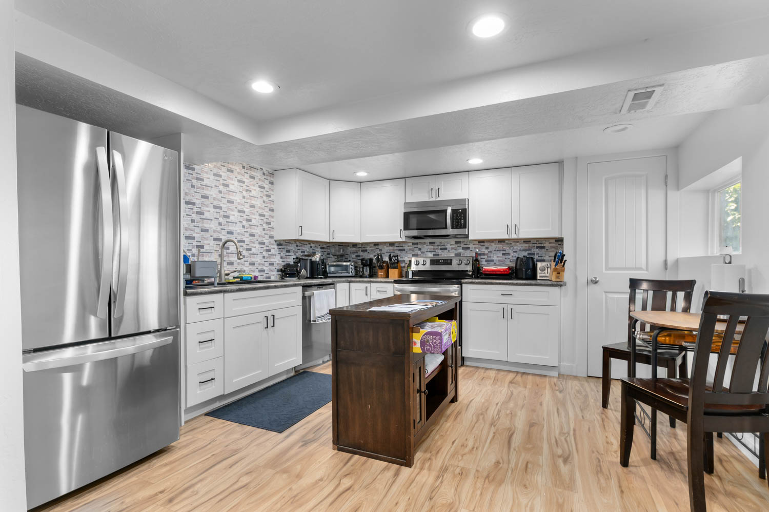 Kitchen featuring wood-finish flooring, white cabinetry, stainless steel appliances, and a mosaic tile backsplash