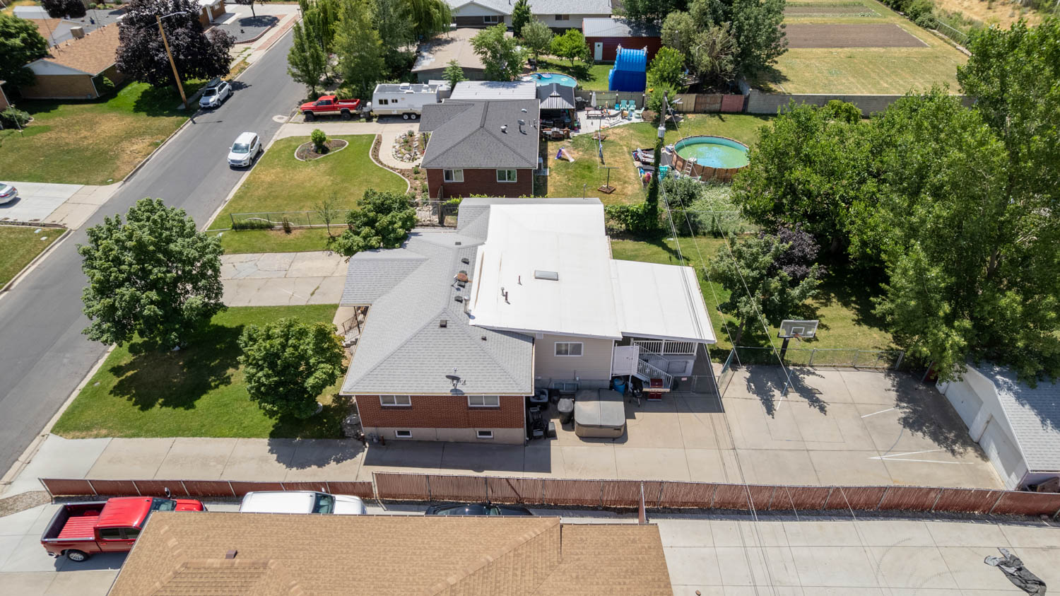 Brick and siding residence with a covered patio, paved driveway, mature trees, and a gravel parking area