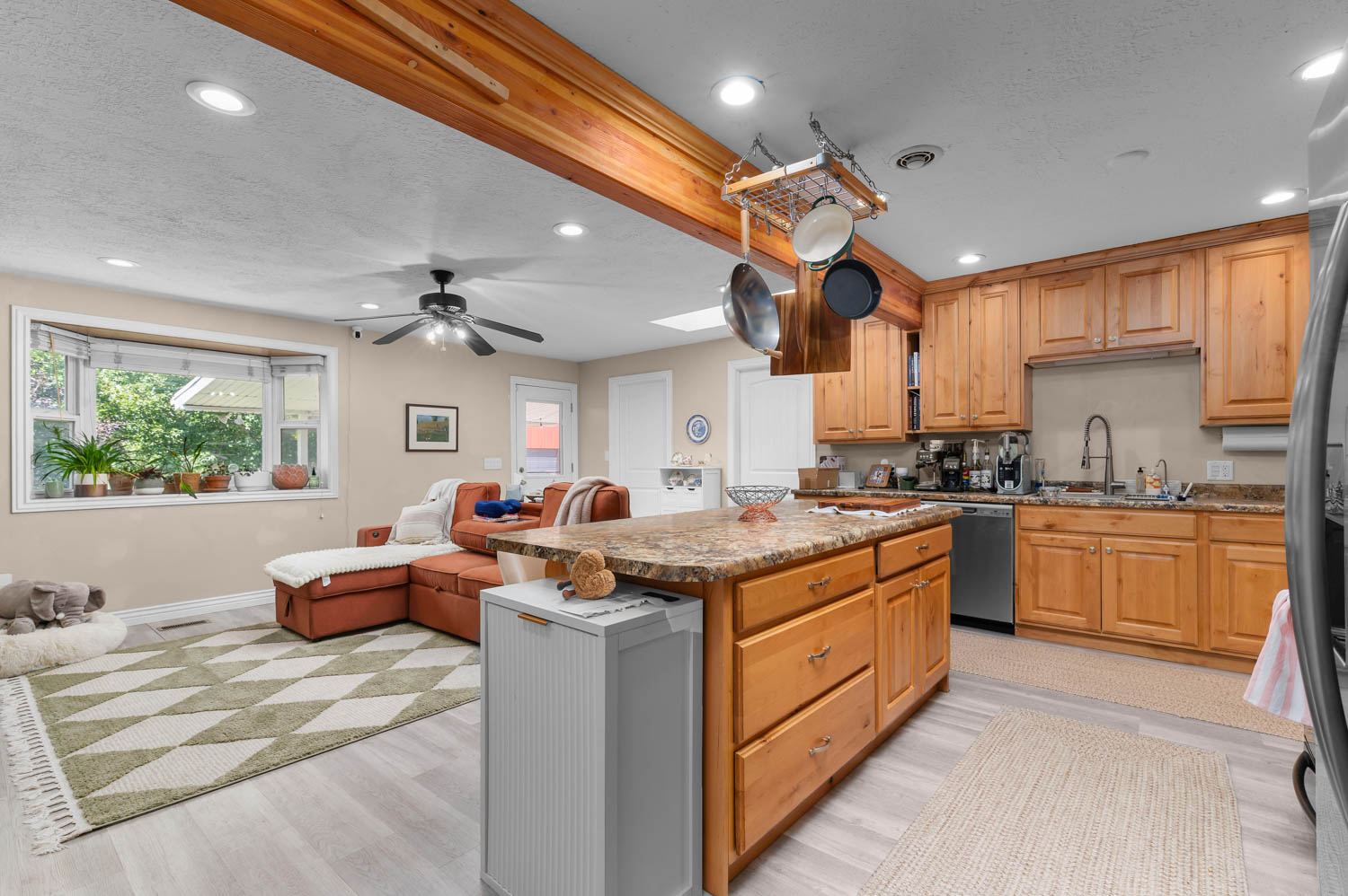 Open concept living space featuring a kitchen island with stone-finish countertop, wood cabinetry, stainless steel appliances, and wood-finish flooring