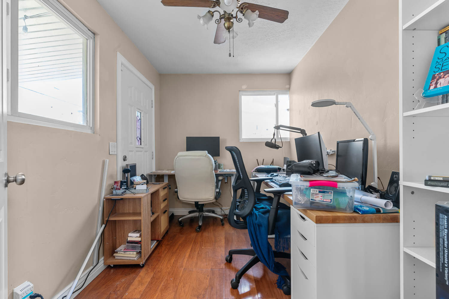 Versatile room featuring wood-finish flooring, two windows, and a ceiling fan with light fixture