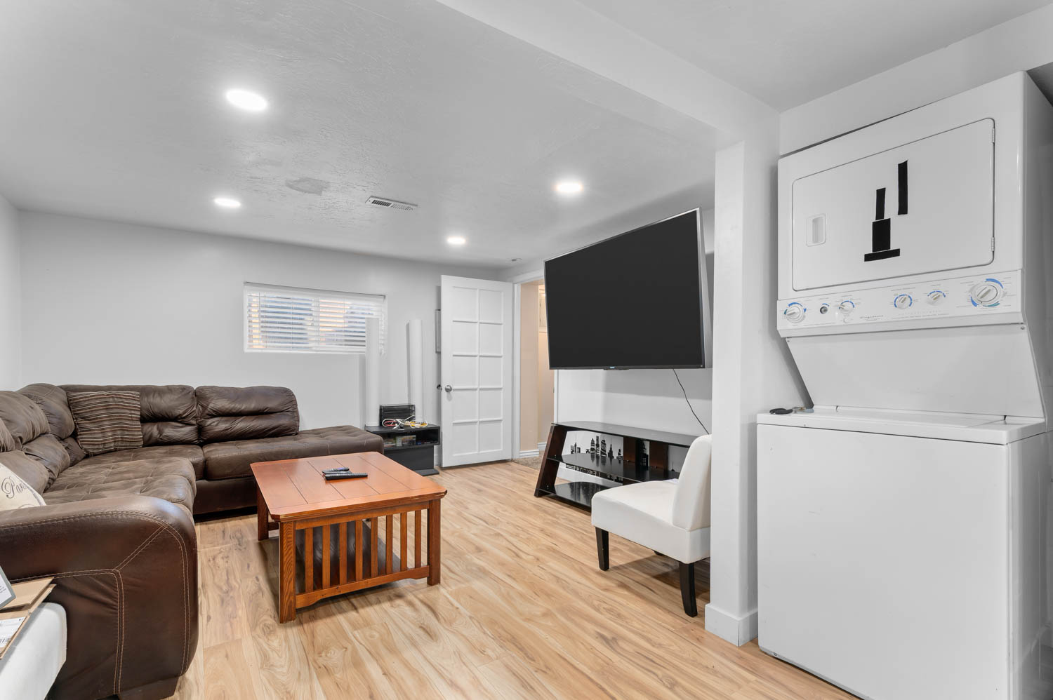 Recessed lighting illuminates this room featuring wood-finish flooring, a white paneled door, and a window with horizontal blinds