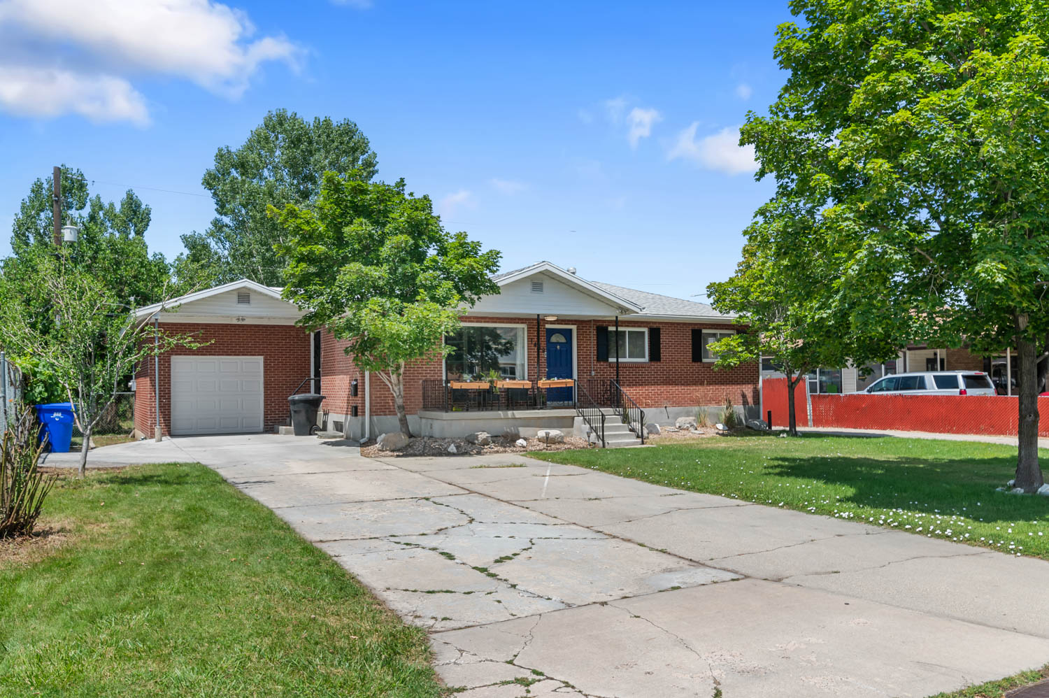 Brick exterior residence with an attached garage, a paved driveway, and mature landscaping