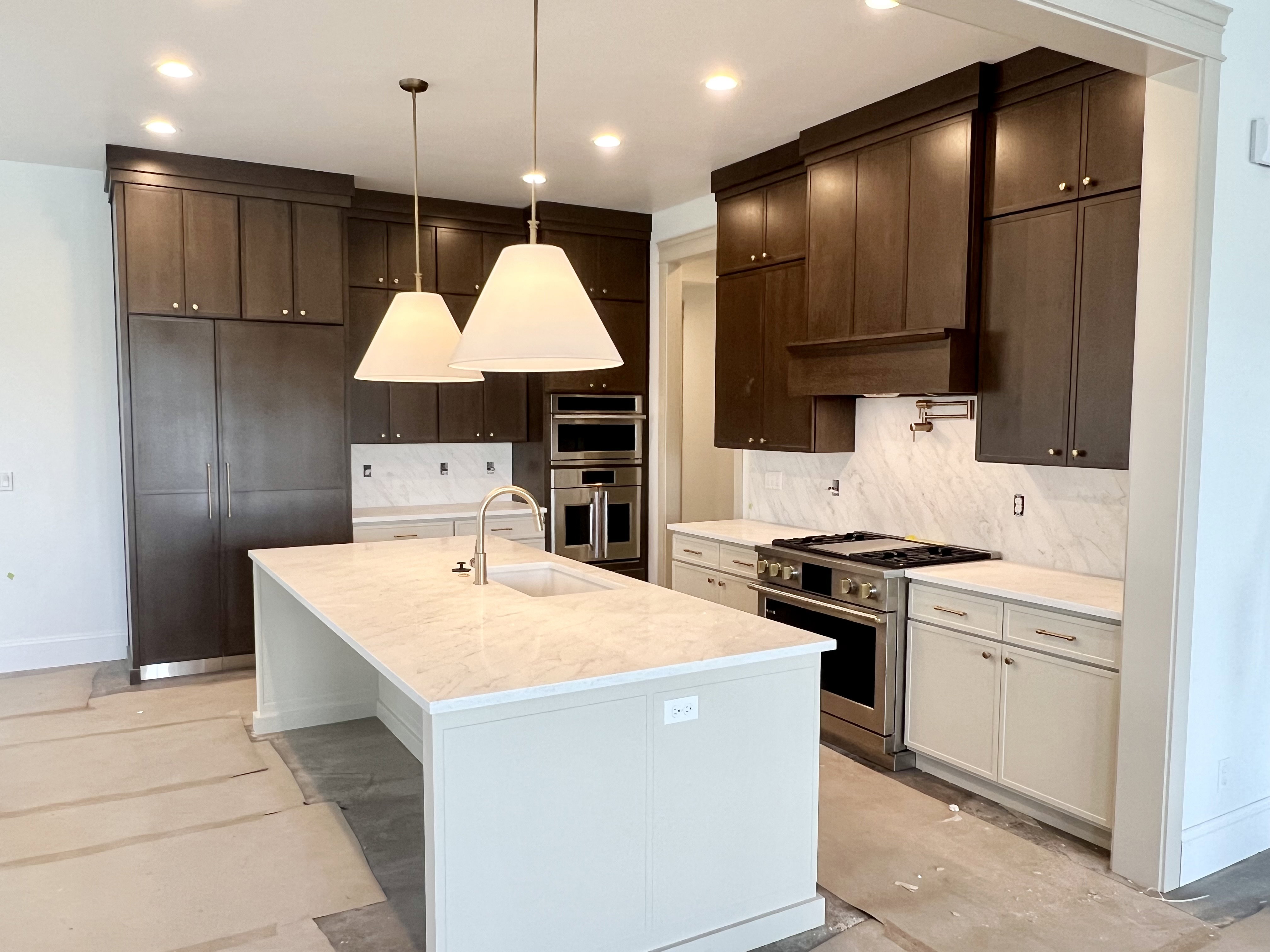 Modern kitchen featuring a large central island with an undermount sink, dark wood upper cabinetry, and contrasting light-toned lower cabinetry