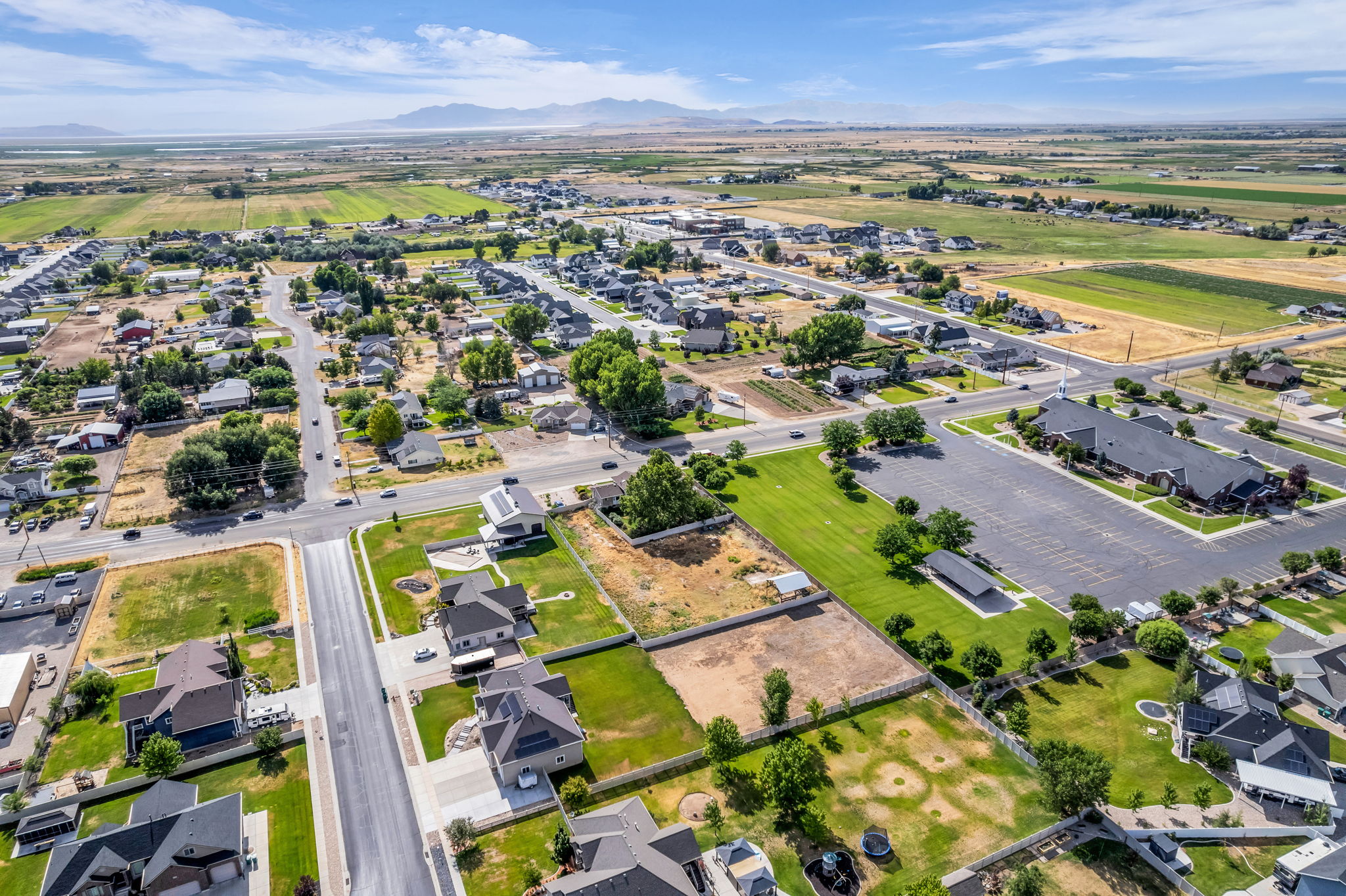 Expansive aerial of a residential area with various property types, featuring paved roads, green lawns, and distant mountains