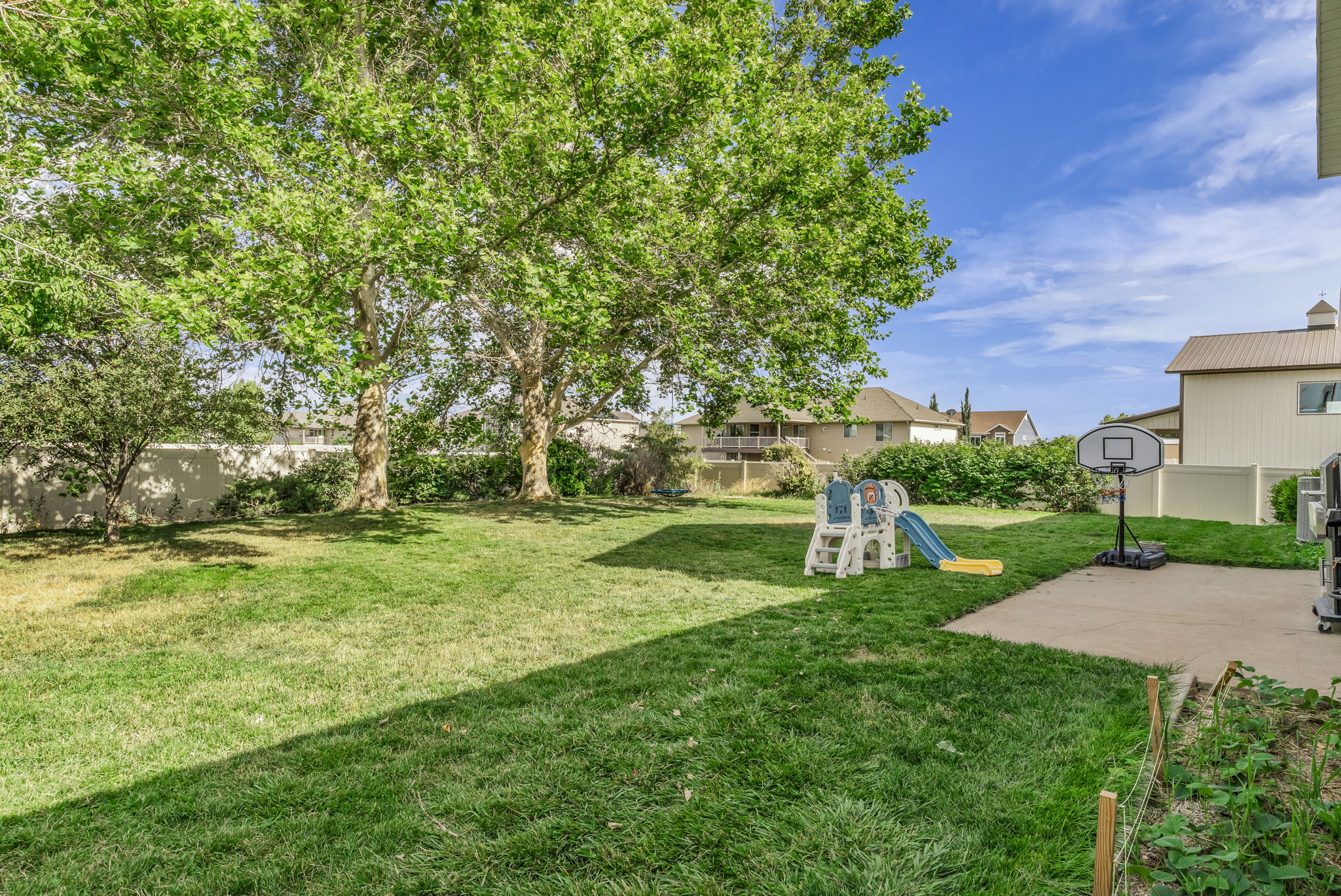 Expansive green lawn featuring mature trees and a concrete patio