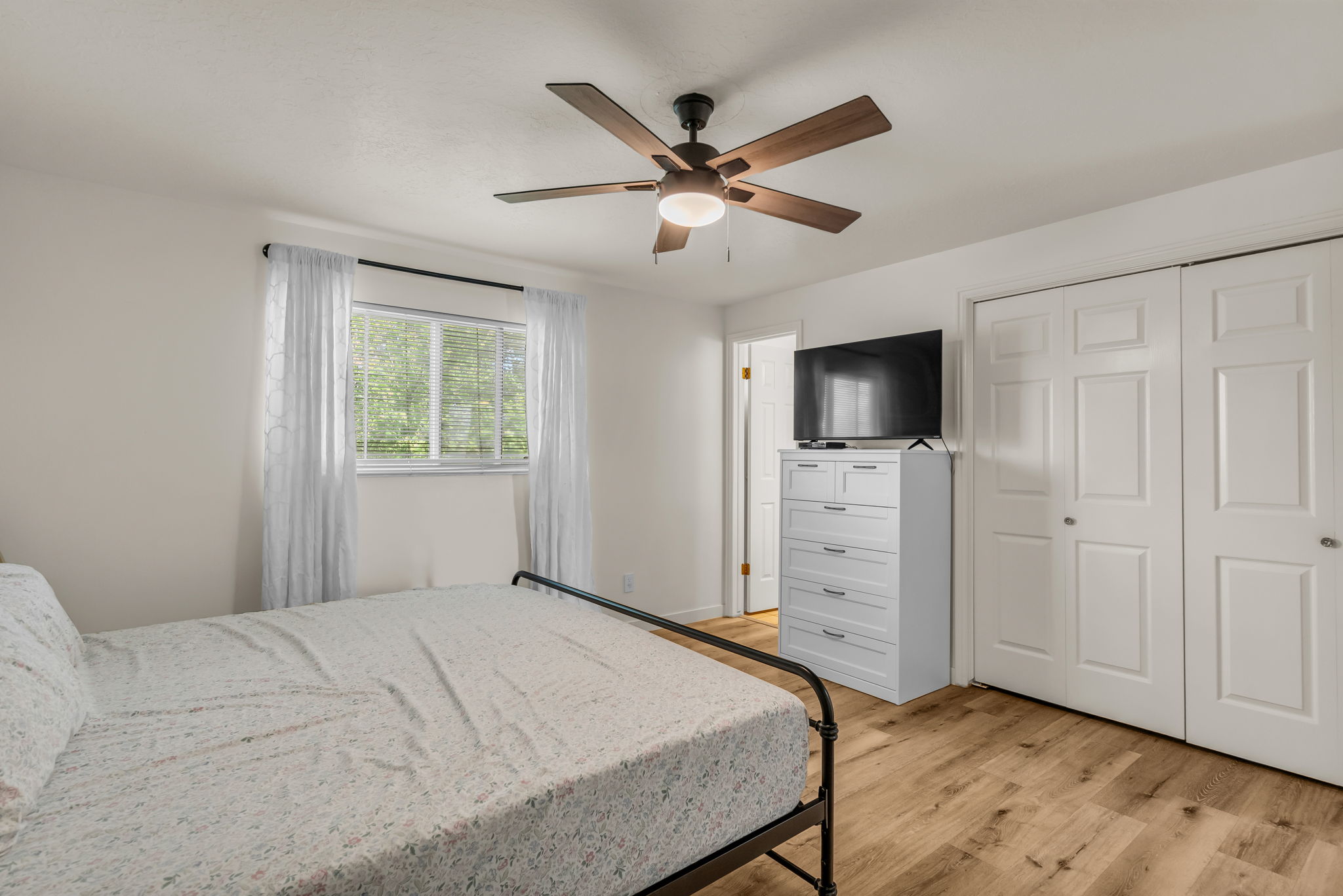 Bedroom featuring wood-finish flooring, a ceiling fan with integrated lighting, a double bi-fold closet, and a window with white trim