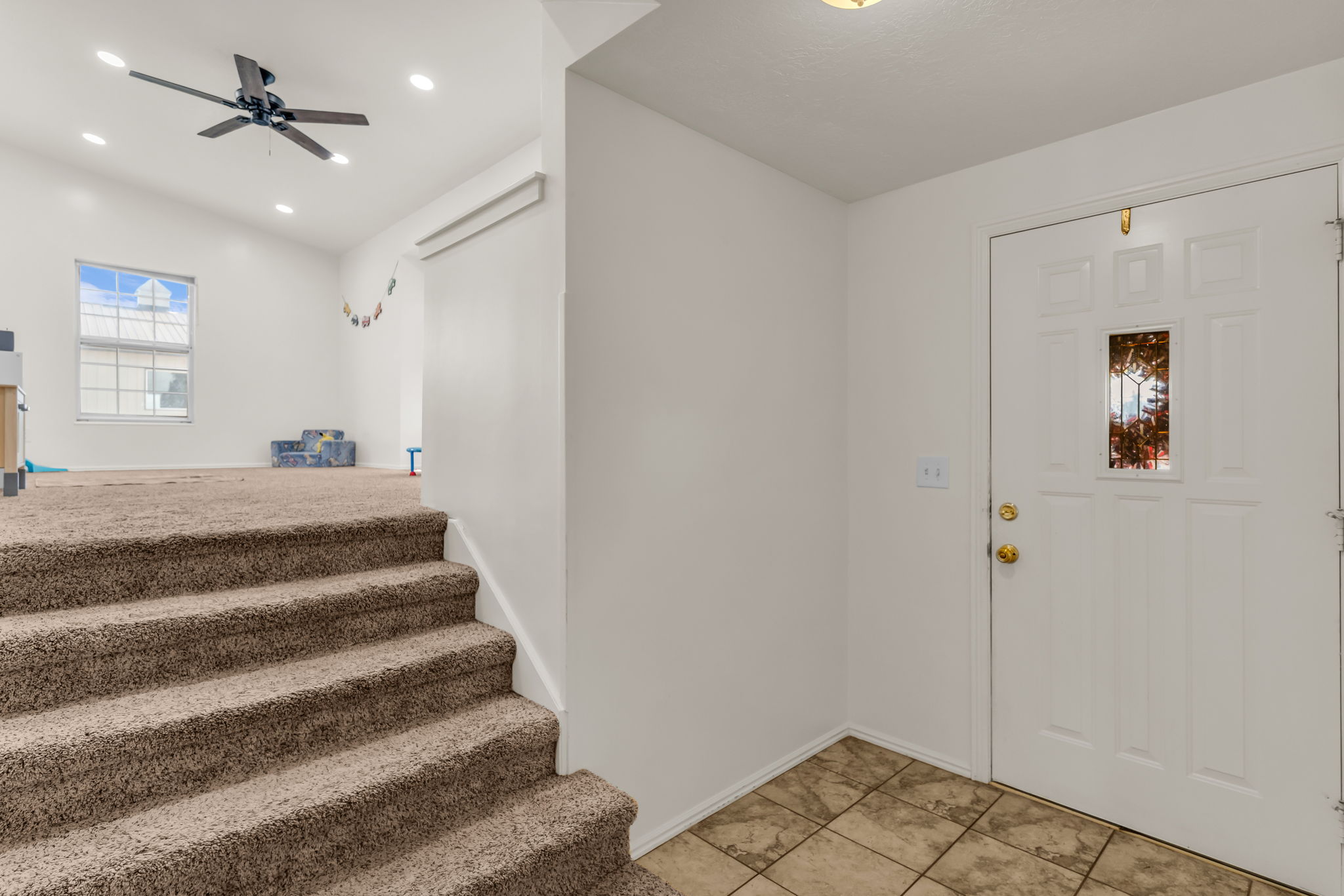 Entryway featuring a paneled door with decorative glass, tiled flooring, and a carpeted staircase leading to an upper level with a ceiling fan and recessed lighting