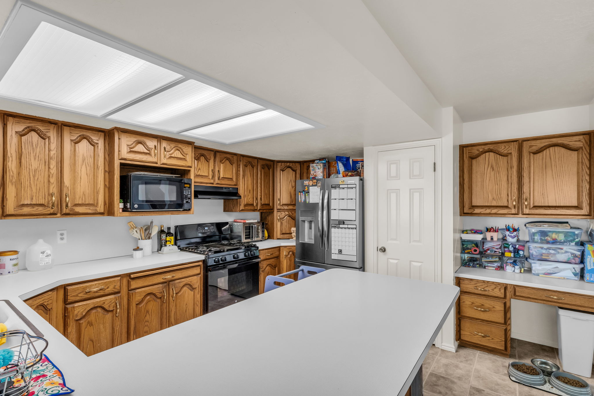 Kitchen featuring wood cabinetry, white countertops, a built-in microwave, a black gas range, and a breakfast bar