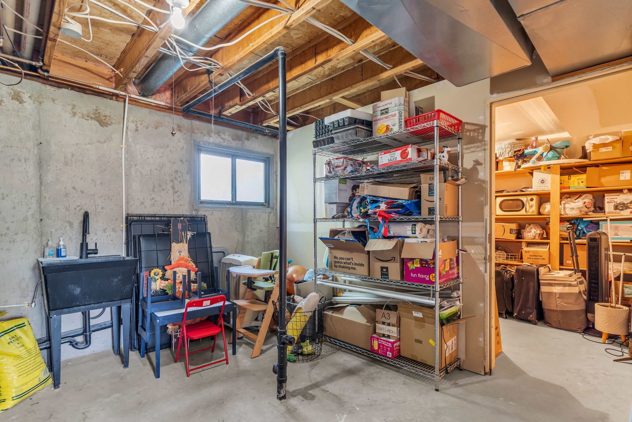 Unfinished basement offering exposed ceiling joists, concrete flooring, a utility sink with a wall-mounted faucet, and a high window