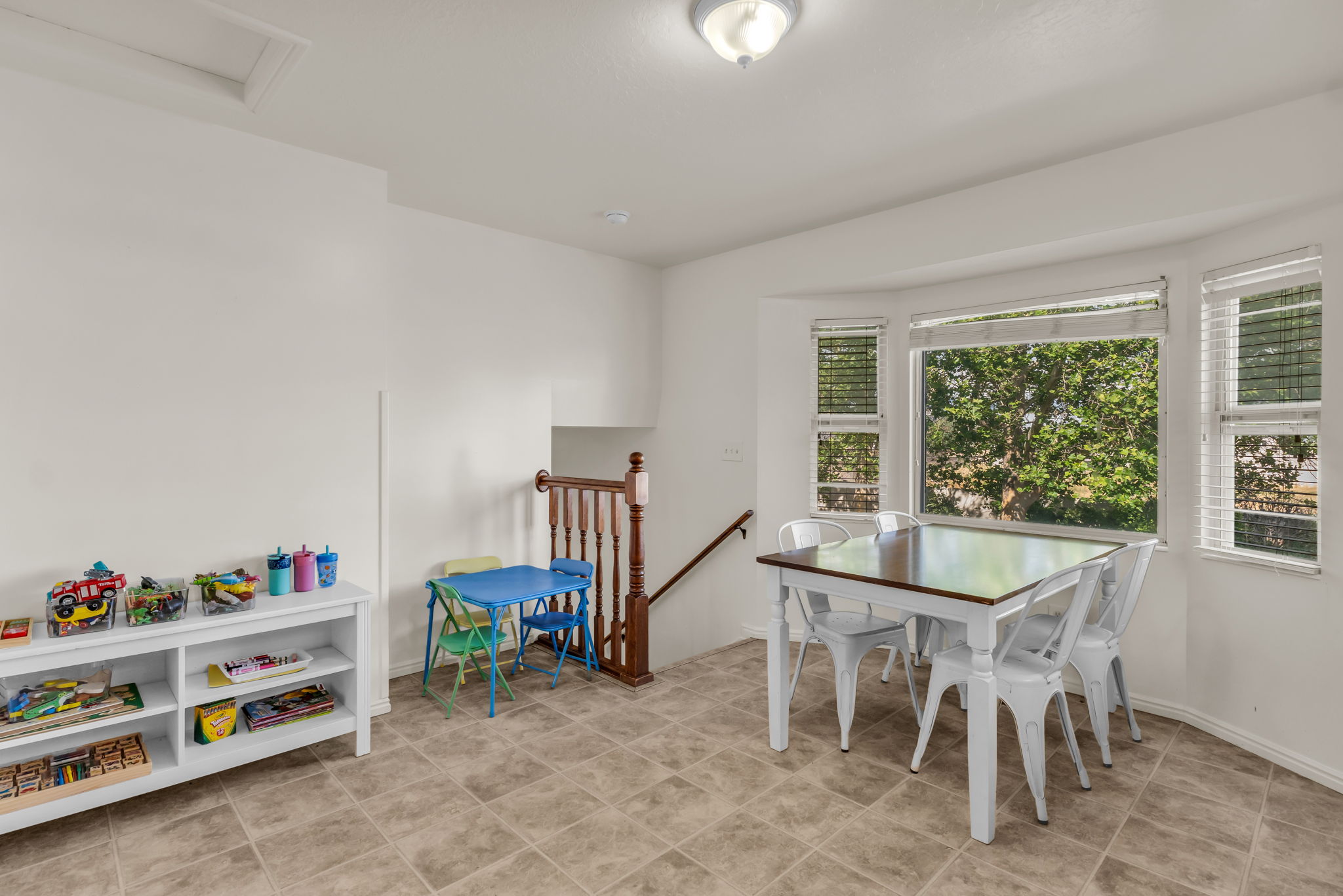 Bright interior space featuring a bay window, neutral tile flooring, a staircase with wood railing, and a flush mount ceiling light