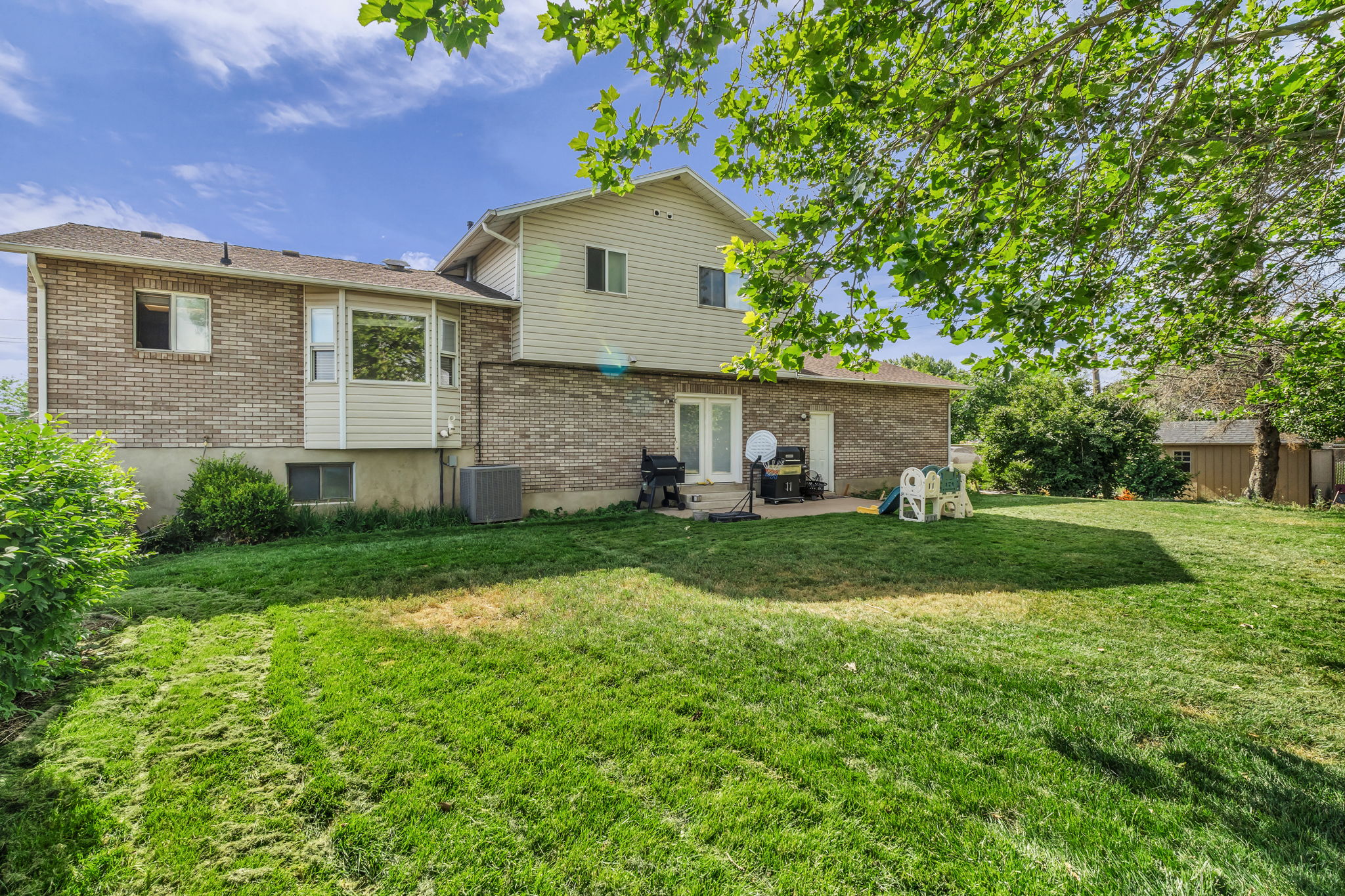 Spacious rear yard with a manicured lawn, established landscaping, and mature trees