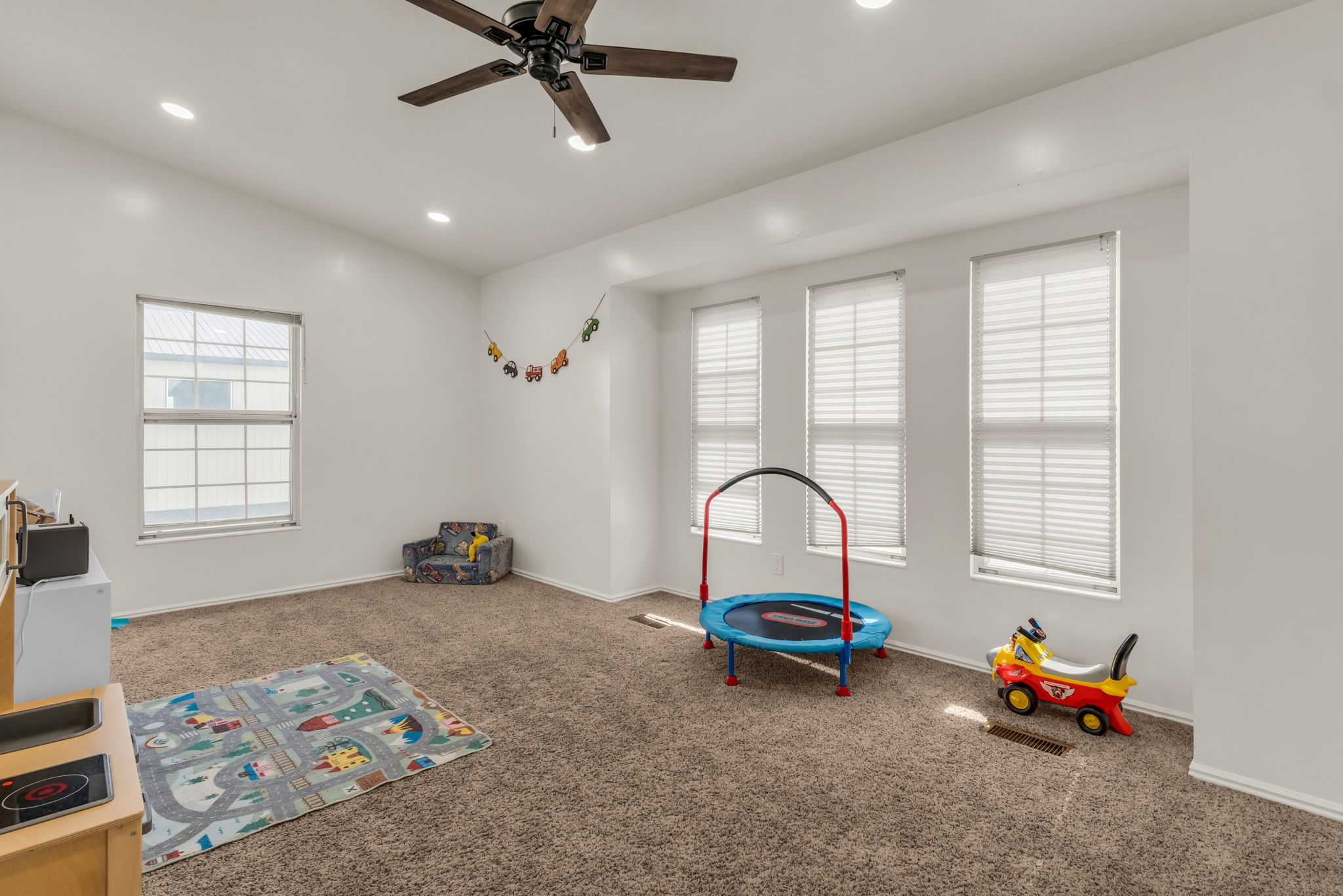 Spacious room featuring neutral carpeting, recessed lighting, and a dark wood-finish ceiling fan