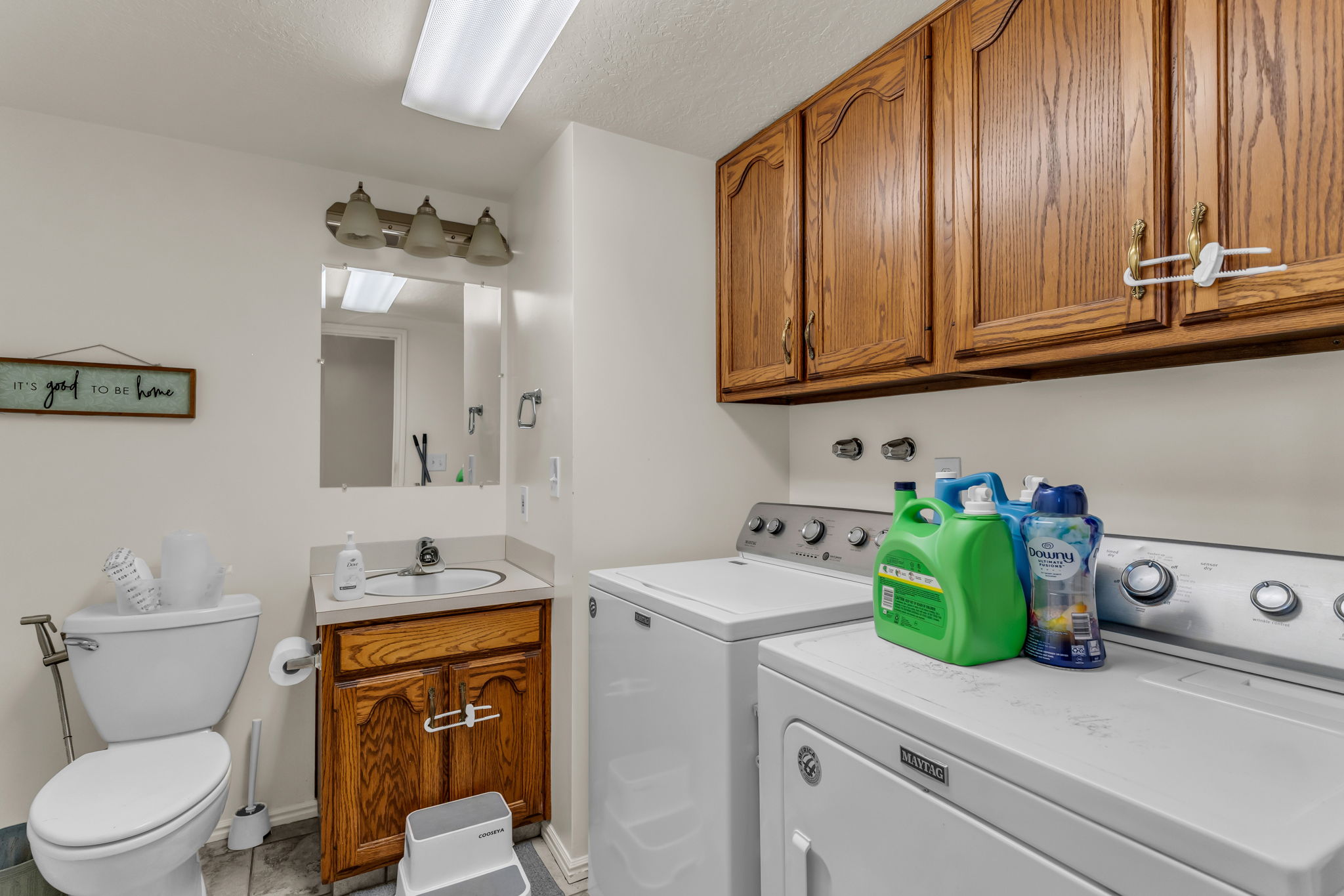 Functional laundry area with wood-finish upper cabinetry, a utility sink with a wood-finish vanity, and overhead lighting