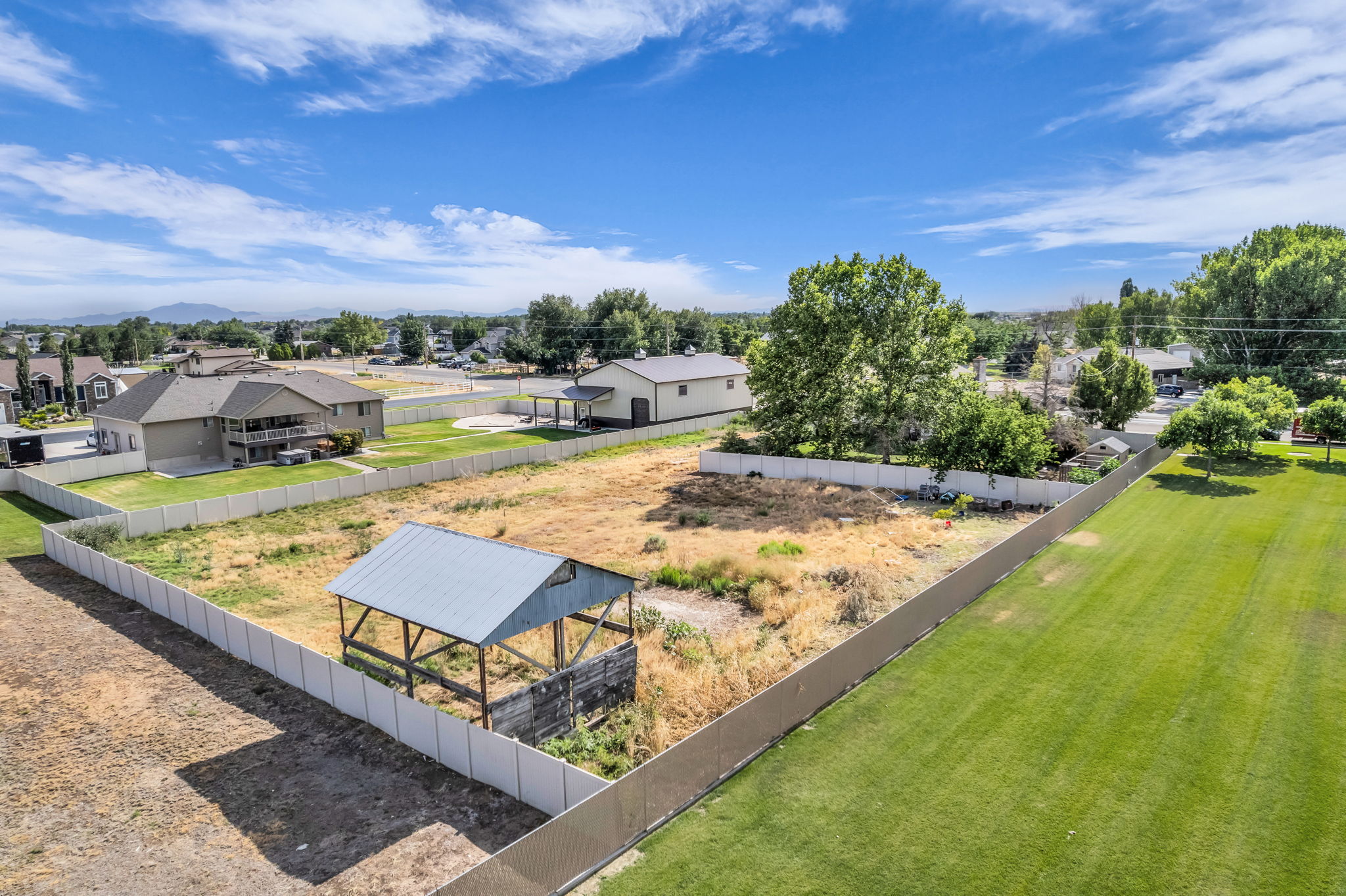 Expansive lot featuring a white perimeter fence, a metal-roofed structure, and a clear sky backdrop
