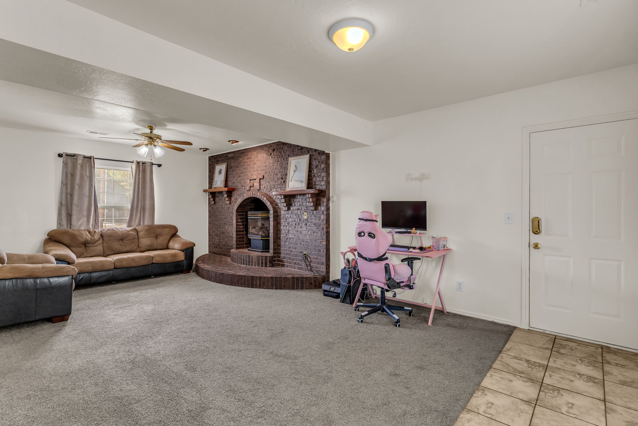 Living area featuring a brick fireplace with a raised hearth, carpet flooring, and a ceiling fan