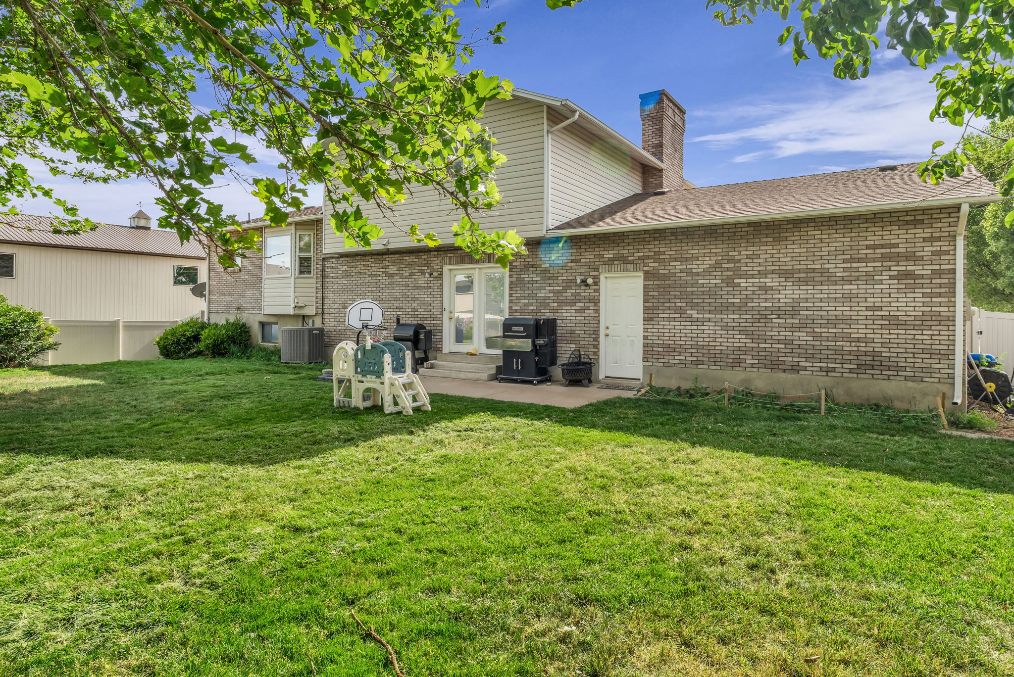 Spacious backyard featuring a large green lawn, a brick and siding exterior, a patio area, and mature trees providing shade