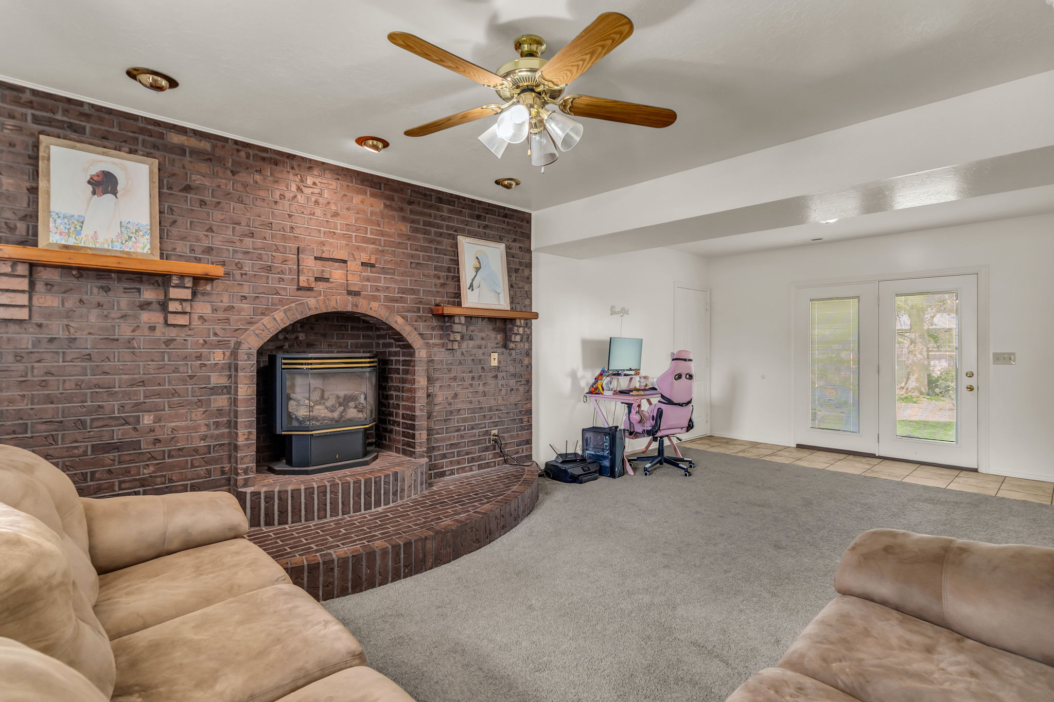 Exposed brick fireplace with a hearth and mantle, recessed lighting, ceiling fan, and double French doors opening to an exterior space