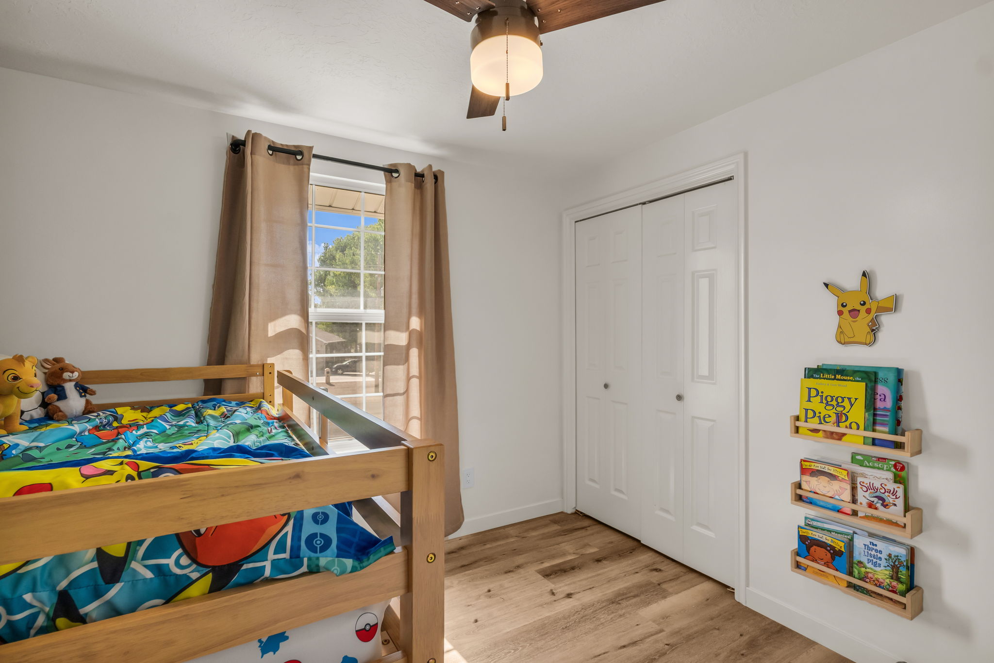 Bright interior room featuring wood-finish flooring, a ceiling fan with integrated lighting, and a window with blinds