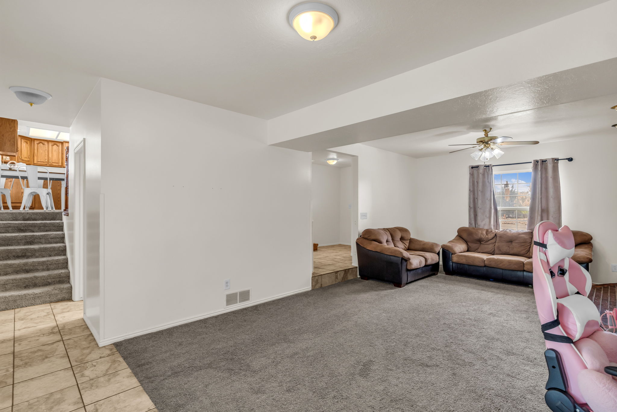 Spacious living area featuring neutral carpeting, white walls, and a ceiling fan