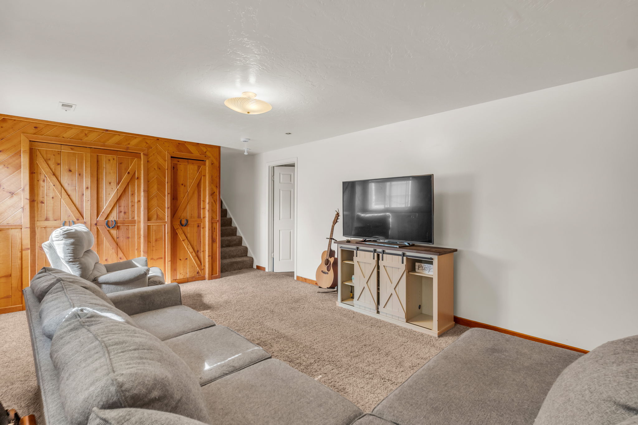 Carpeted room featuring a wood-paneled accent wall with barn-style doors, a carpeted staircase, and a white interior door