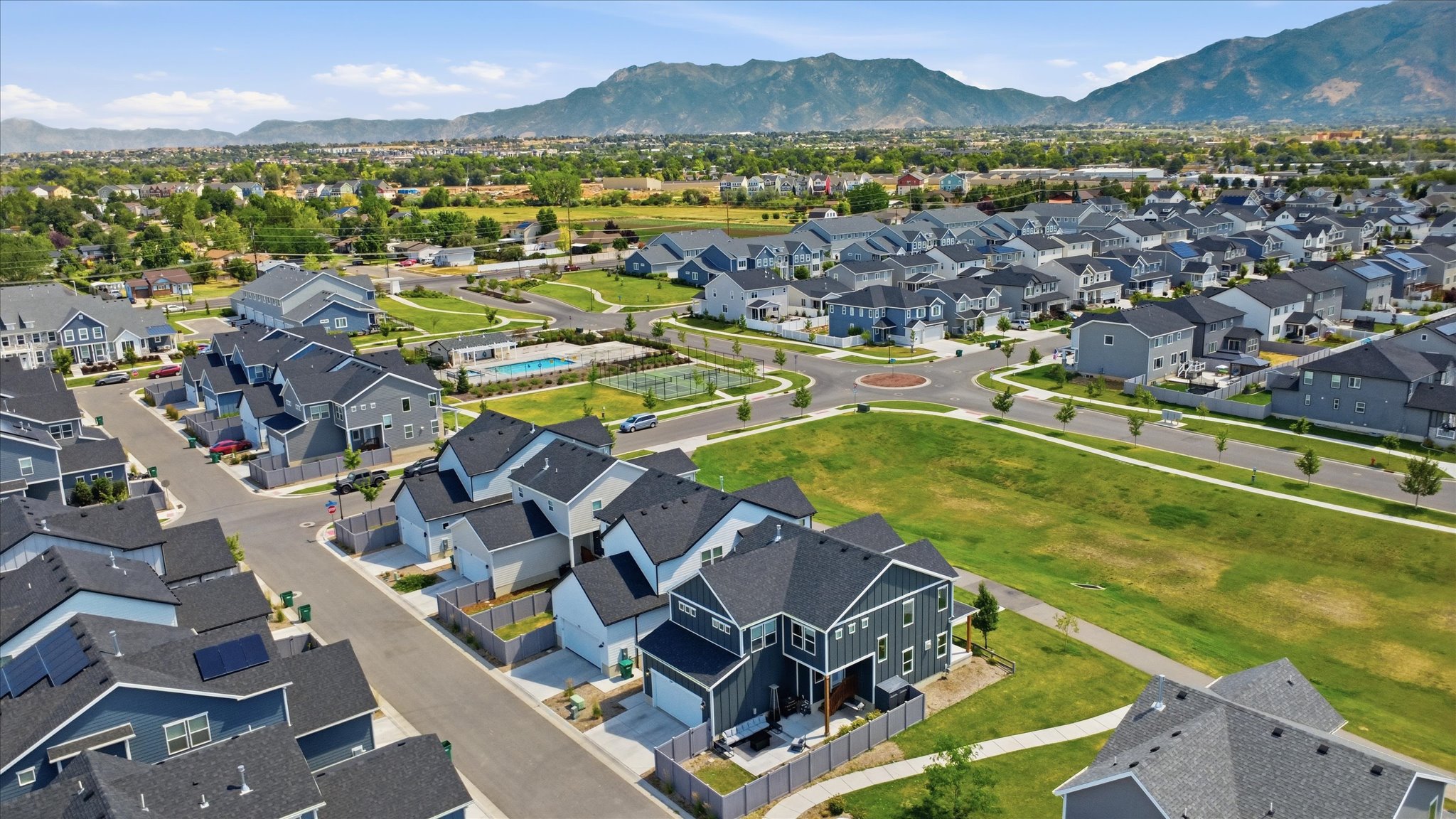 Modern residential development featuring a collection of contemporary homes, a community pool, tennis courts, and expansive green spaces