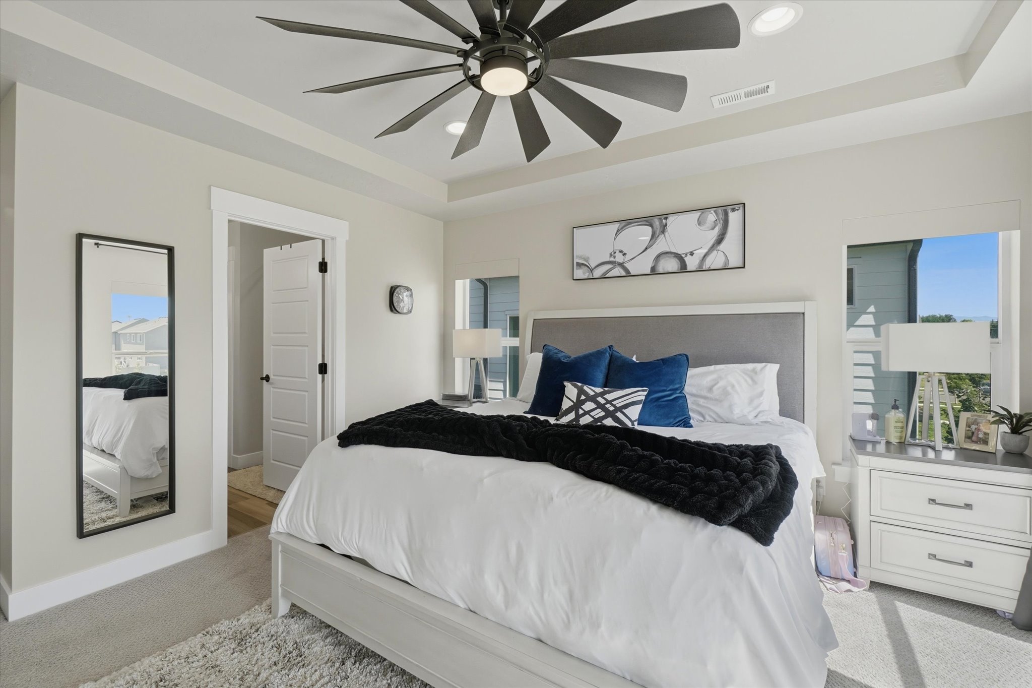 Spacious bedroom featuring a tray ceiling with a dark-finish ceiling fan, recessed lighting, and light gray carpeting