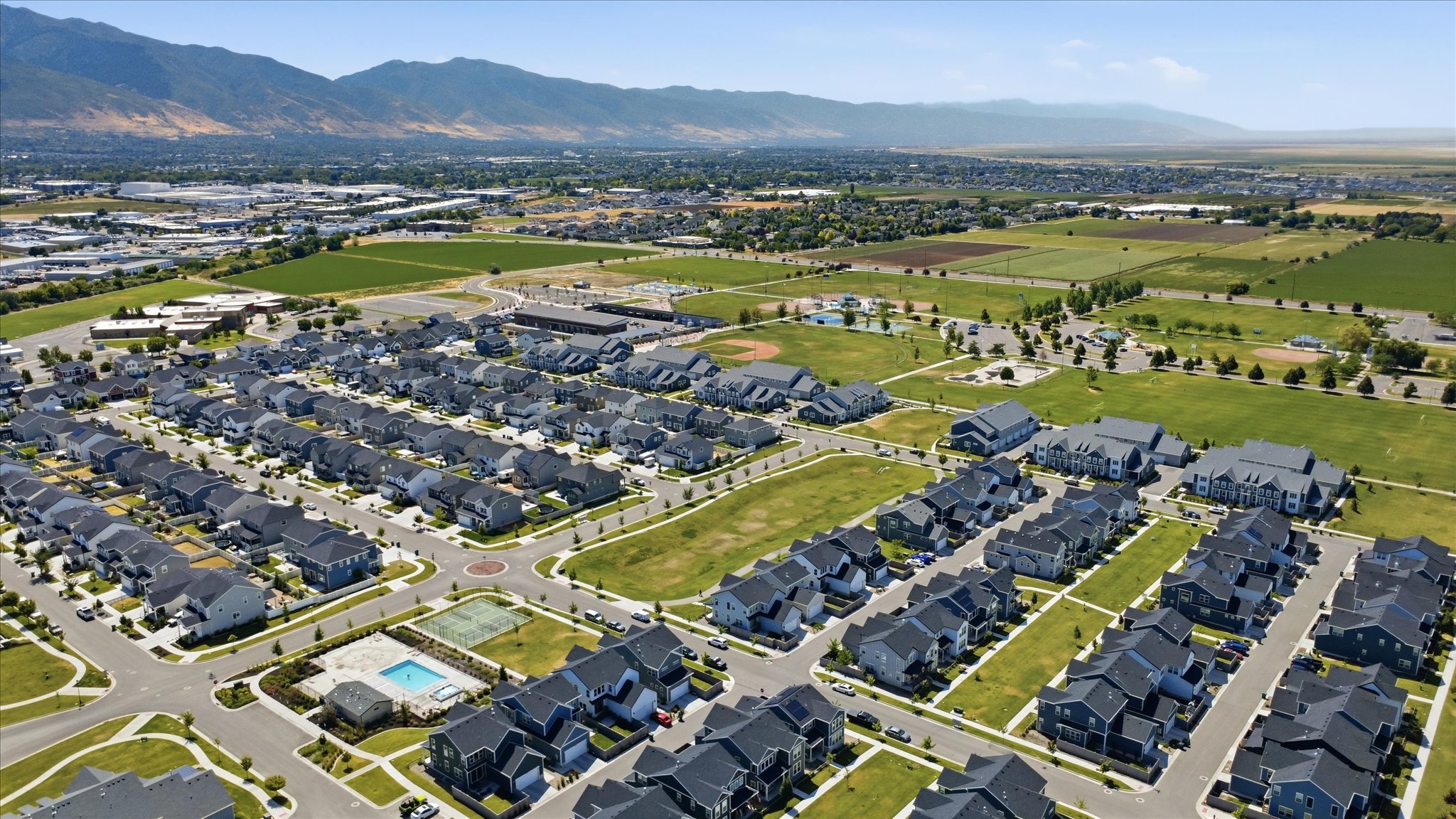 Aerial perspective showcasing a residential development with a community pool, tennis courts, and varied housing styles