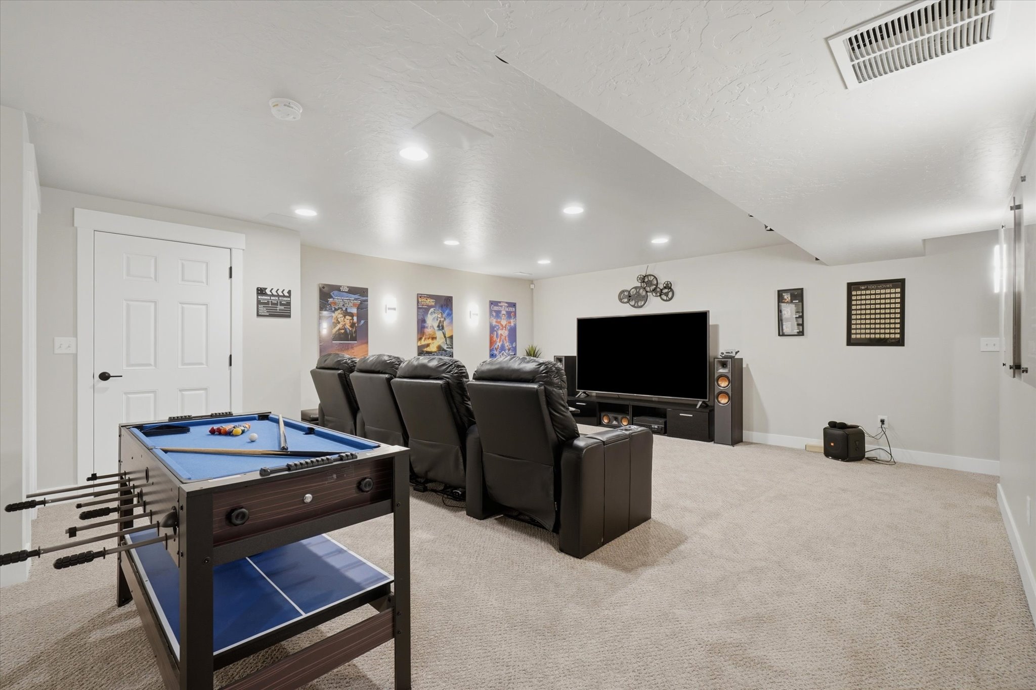 Spacious carpeted entertainment room featuring recessed lighting, a white paneled door, and ample wall space