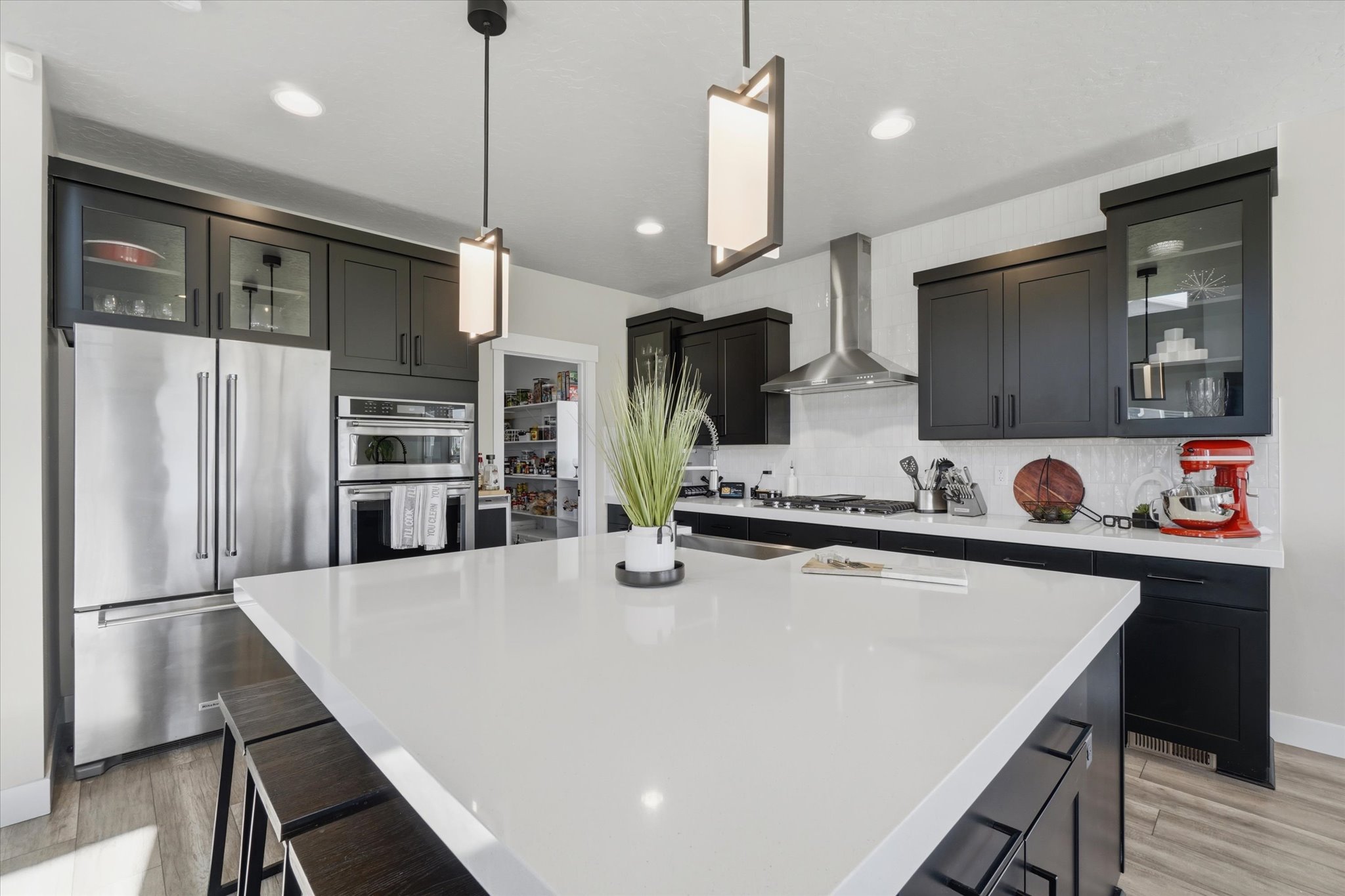 Spacious kitchen featuring a large white island with seating, dark shaker-style cabinetry, stainless steel appliances, and a tiled backsplash
