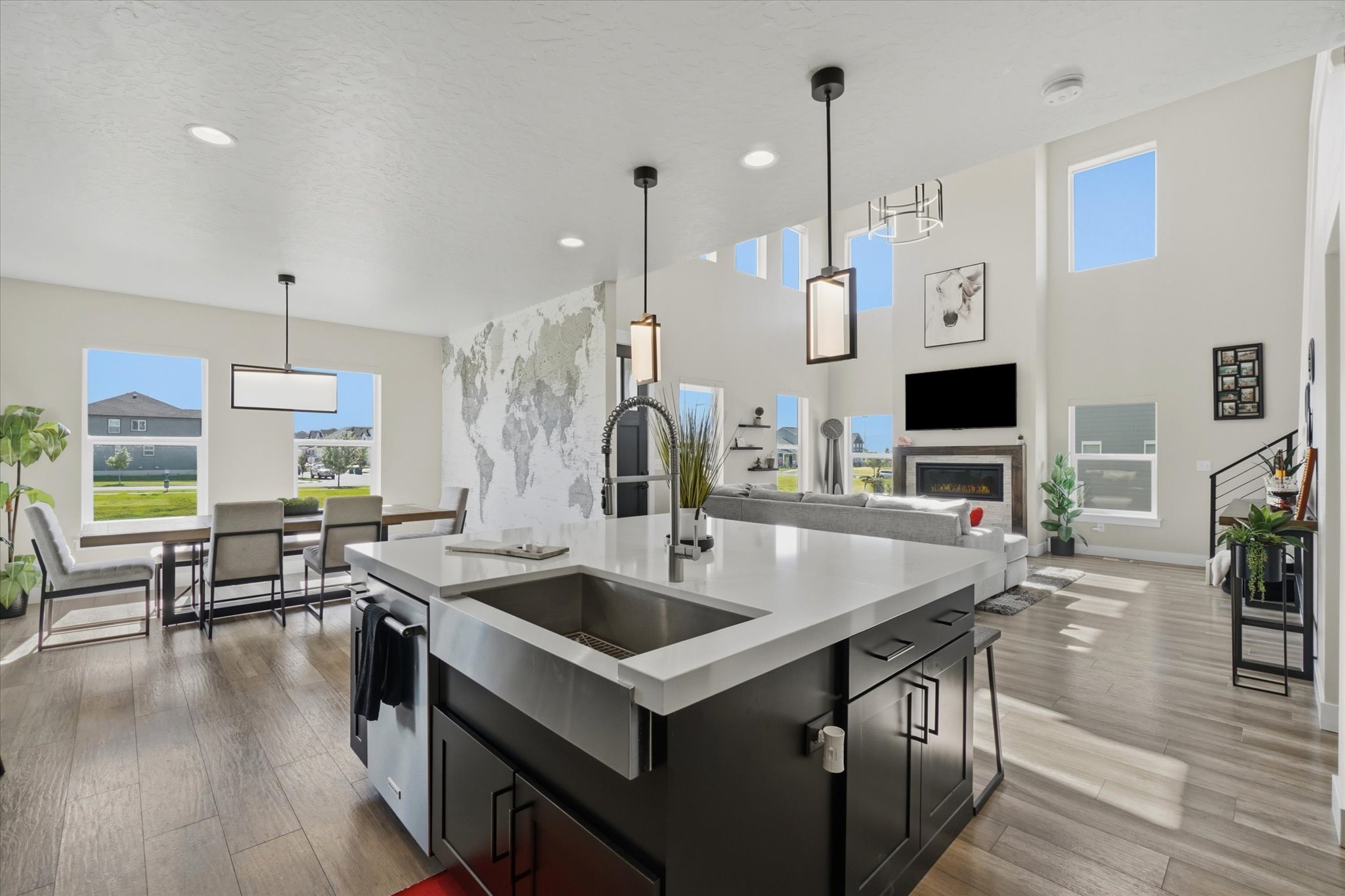 Spacious open-concept living area featuring an expansive kitchen island with a farmhouse sink, high ceilings, and abundant natural light from numerous windows