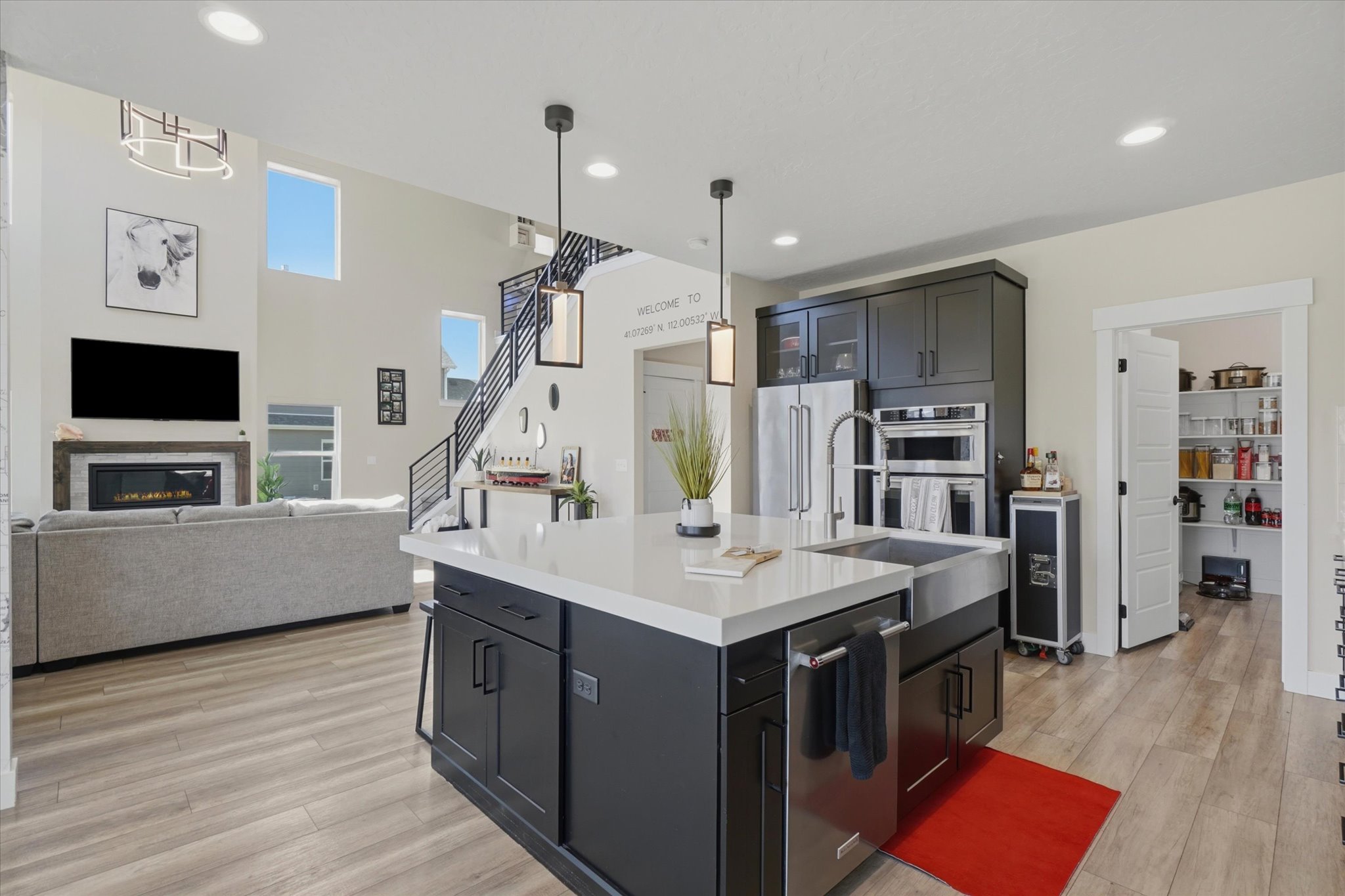 Open-concept kitchen featuring a large island with a farmhouse sink, dark cabinetry, and integrated appliances