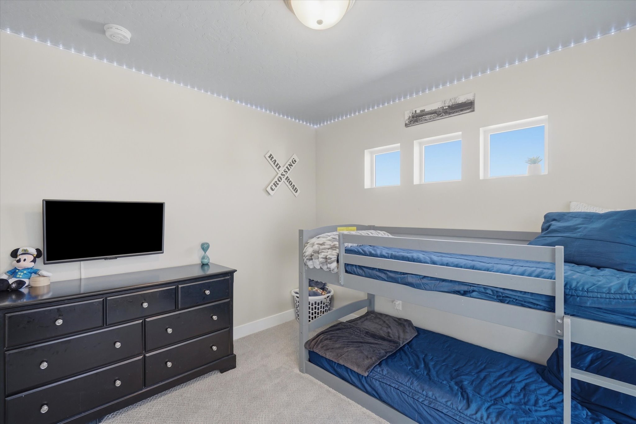 Carpeted room featuring a ceiling-mounted light fixture, three rectangular windows, and a built-in smoke detector