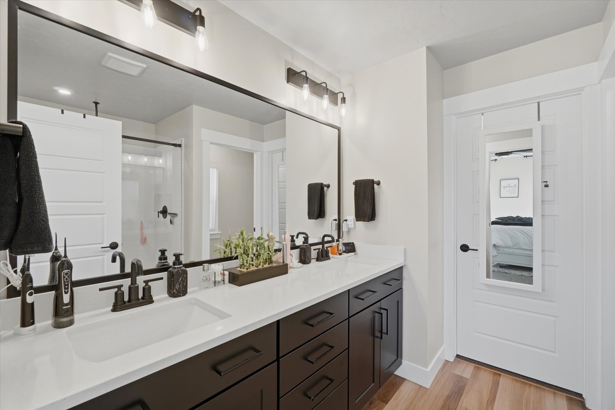 Contemporary bathroom featuring a long vanity with white countertop, dual integrated sinks, dark wood-finish cabinetry, and matte black hardware