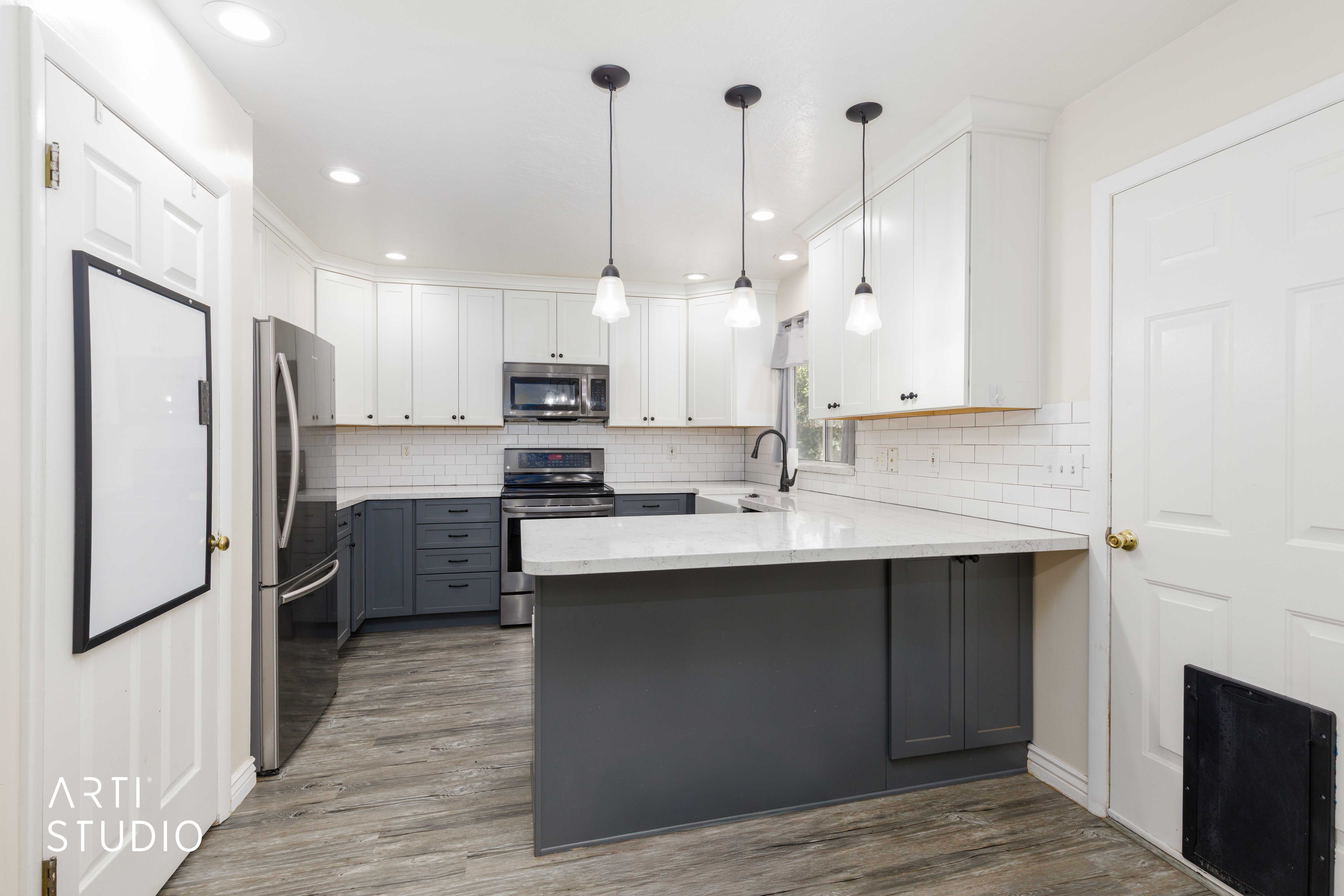 Modern kitchen featuring two-tone cabinetry, stainless steel appliances, wood-finish flooring, white subway tile backsplash, and a central island with a solid surface countertop