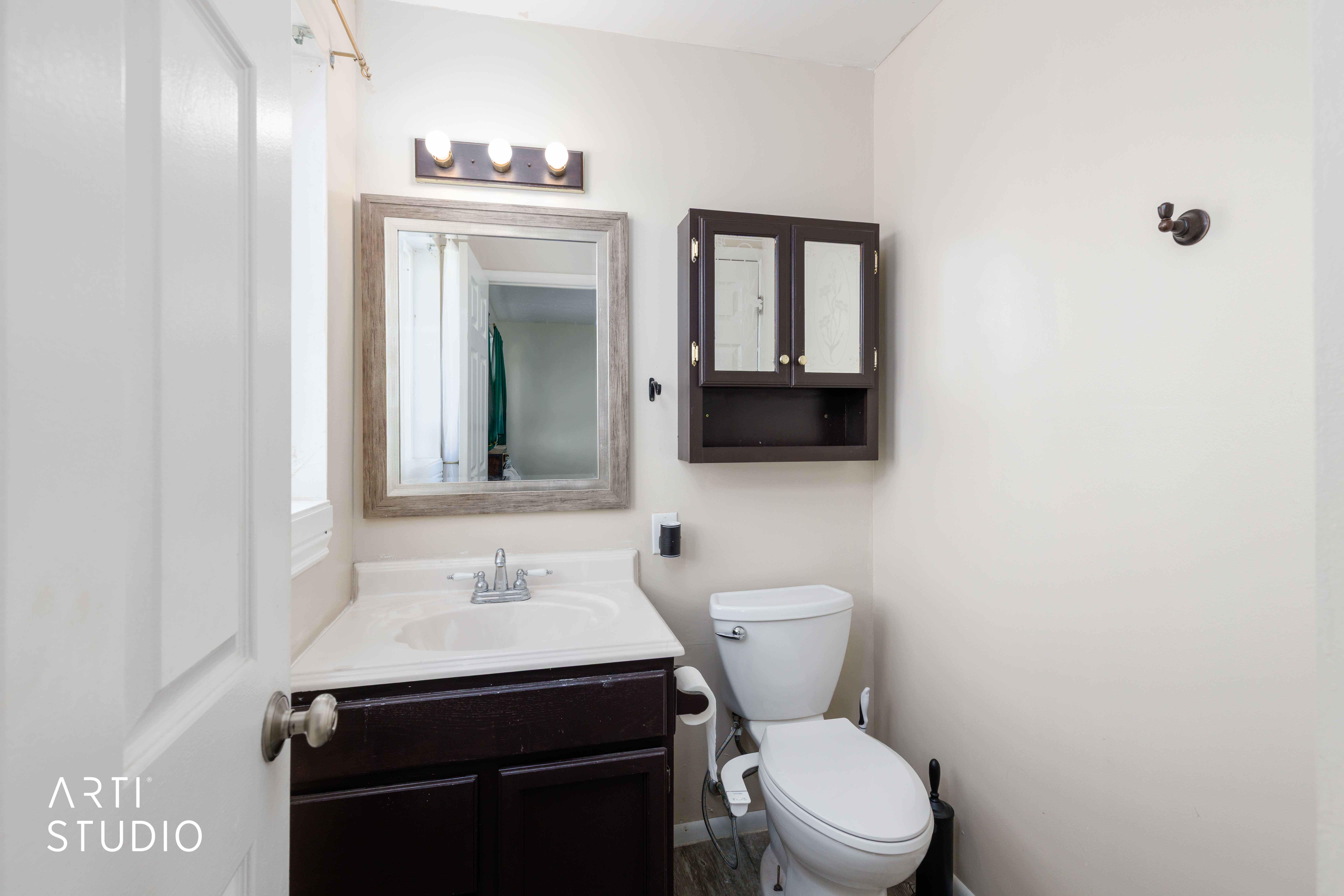 Bathroom featuring a dark wood-finish vanity with an integrated sink, framed mirror, wall-mounted light fixture, and a dark wood-finish medicine cabinet