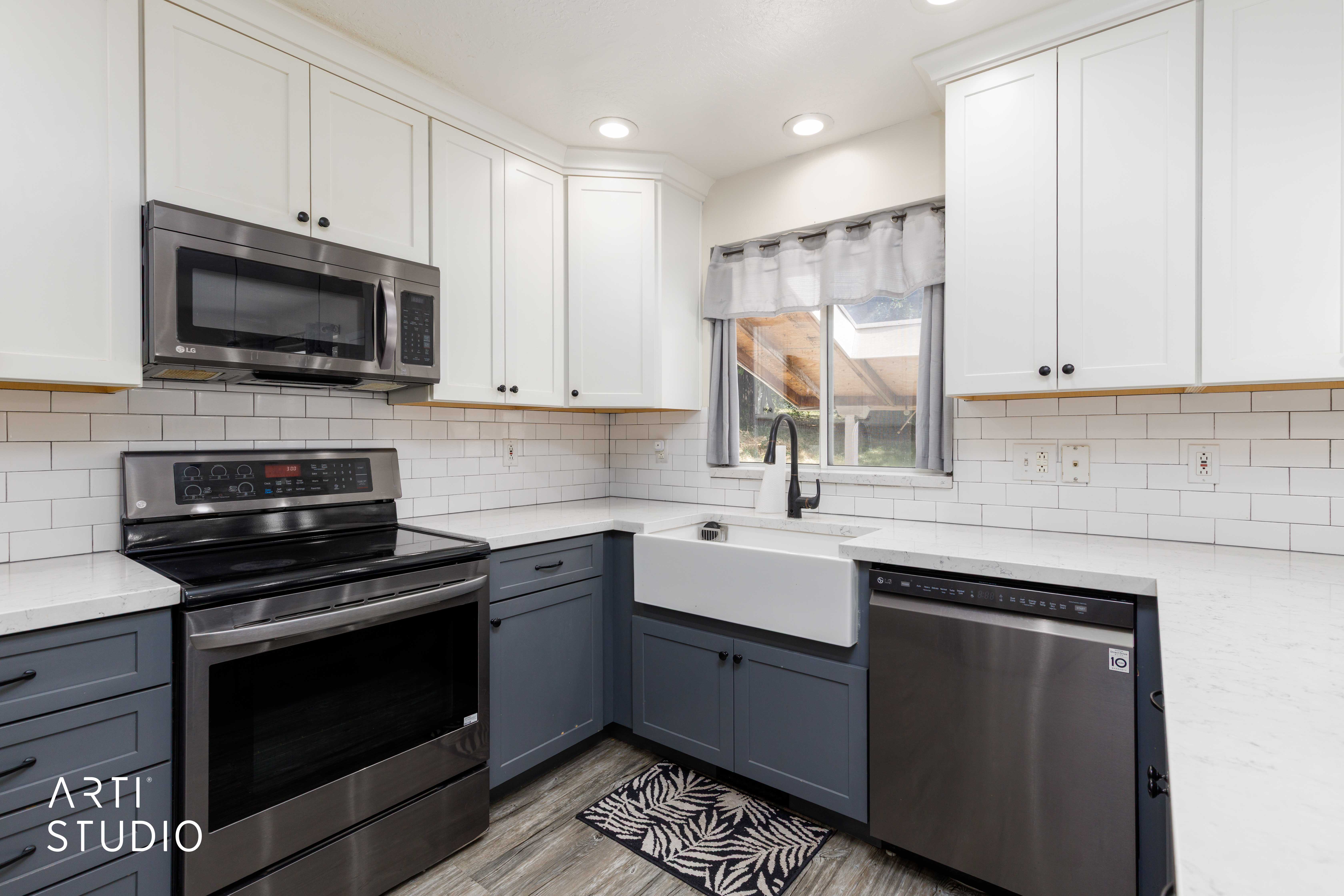 Modern kitchen featuring two-tone cabinetry, stainless steel appliances, a farmhouse-style sink with a matte black faucet, white subway tile backsplash, and light-toned countertops