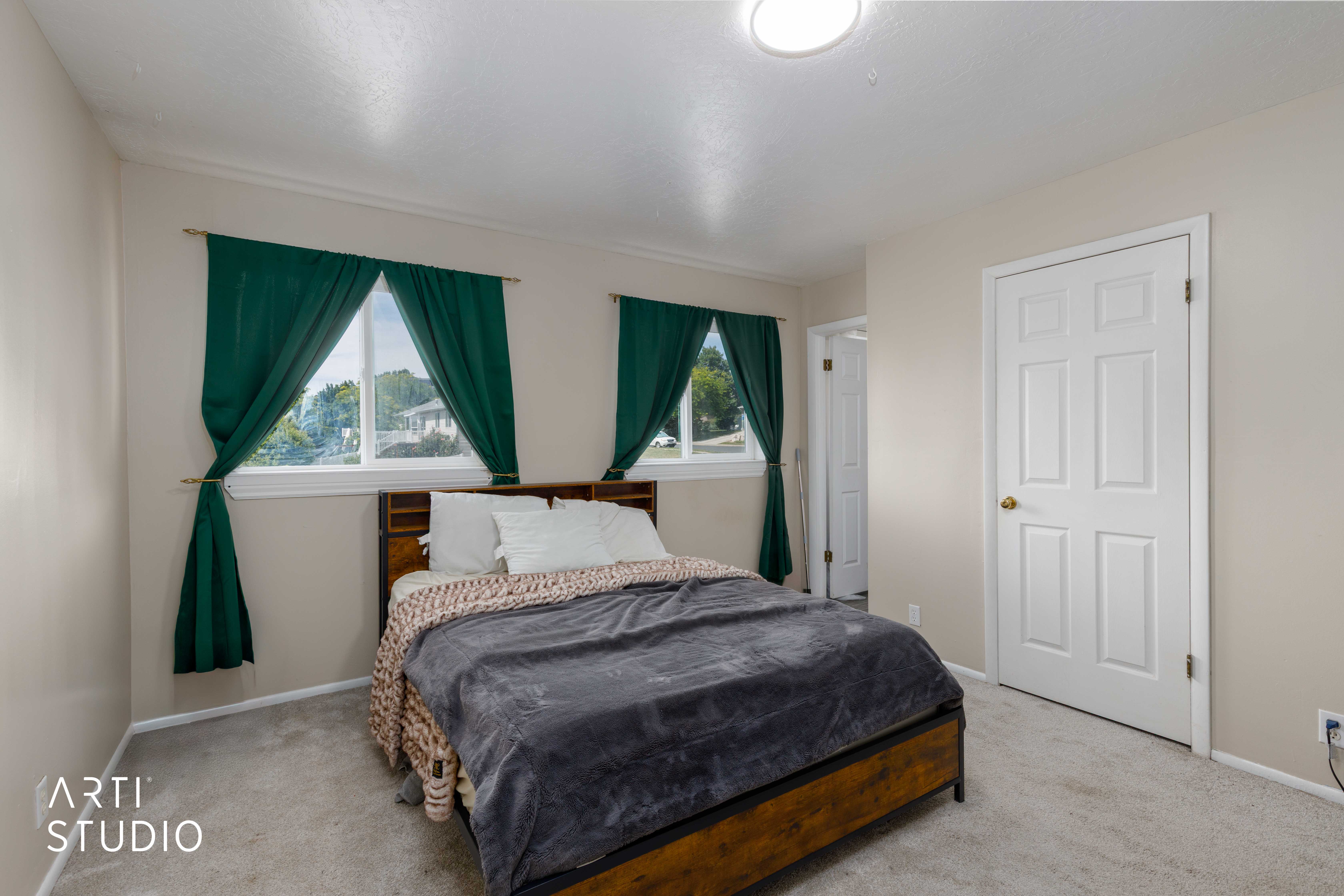 Carpeted bedroom featuring two large windows with white trim, a flush-mount ceiling light fixture, a white six-panel door, and neutral-toned walls