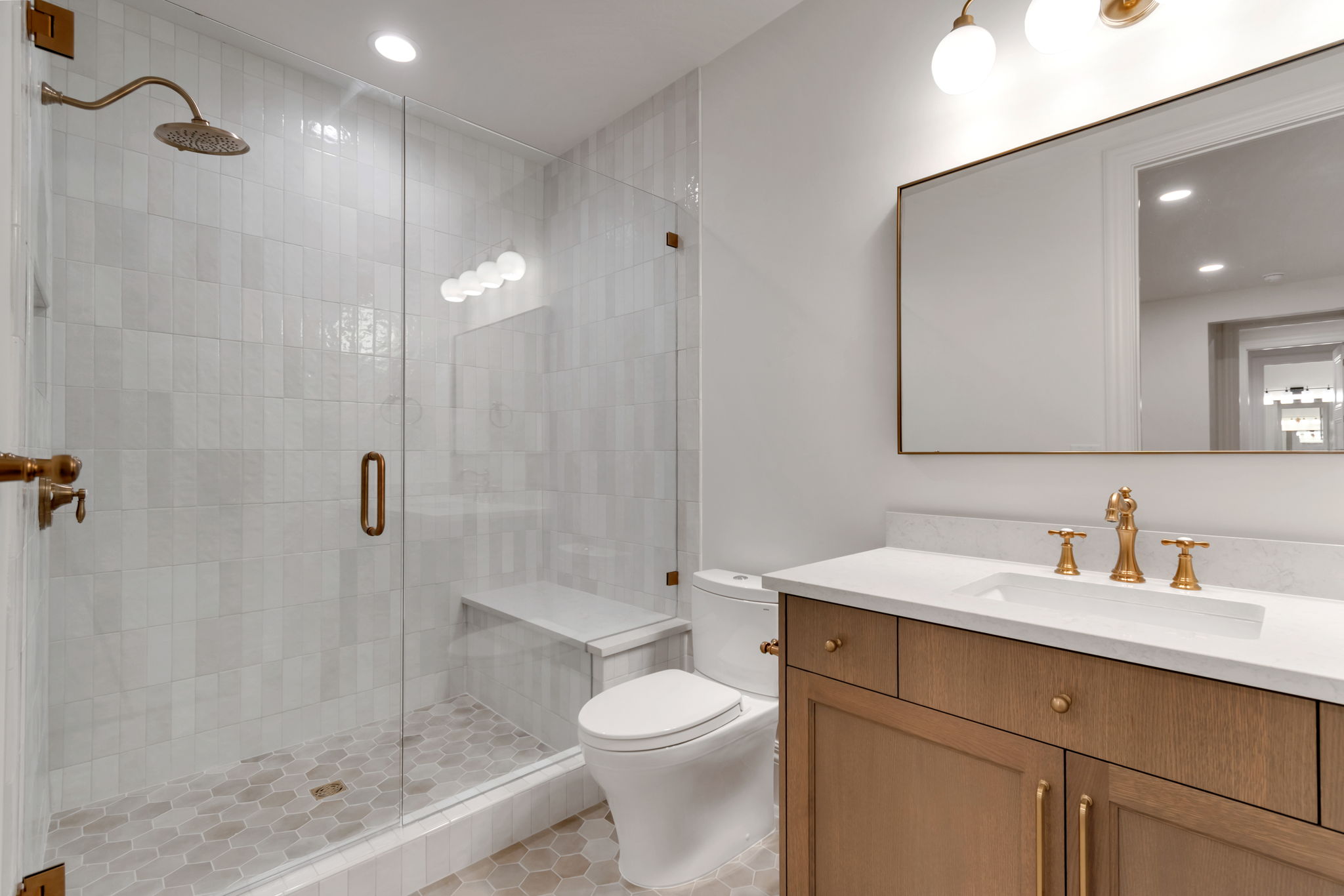 Bathroom featuring a glass-enclosed shower with vertical subway tile, a built-in shower bench, and a brass rain showerhead