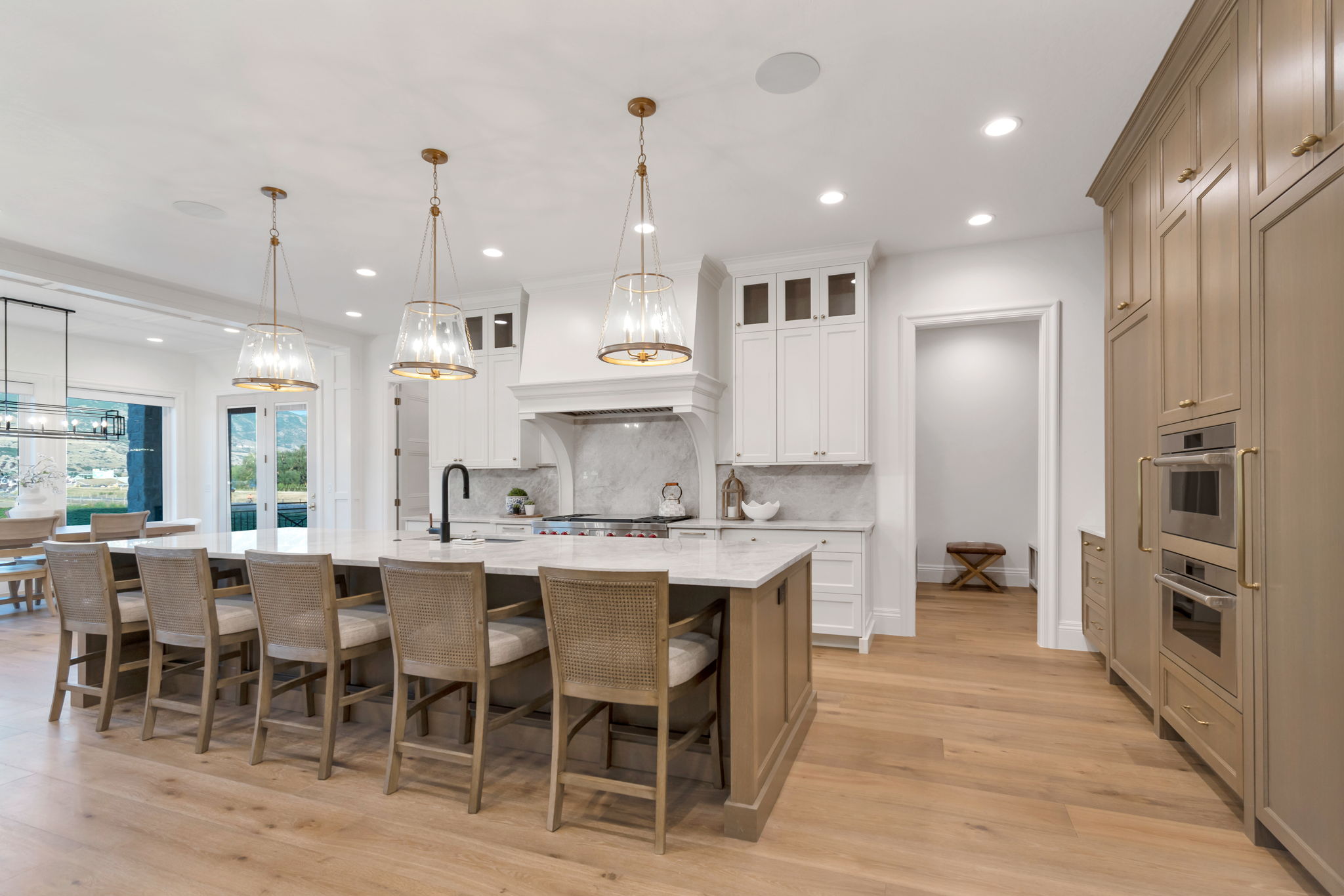 Gourmet kitchen featuring a large central island with seating, natural wood-finish flooring, white and natural wood-tone cabinetry, built-in double ovens, and recessed lighting