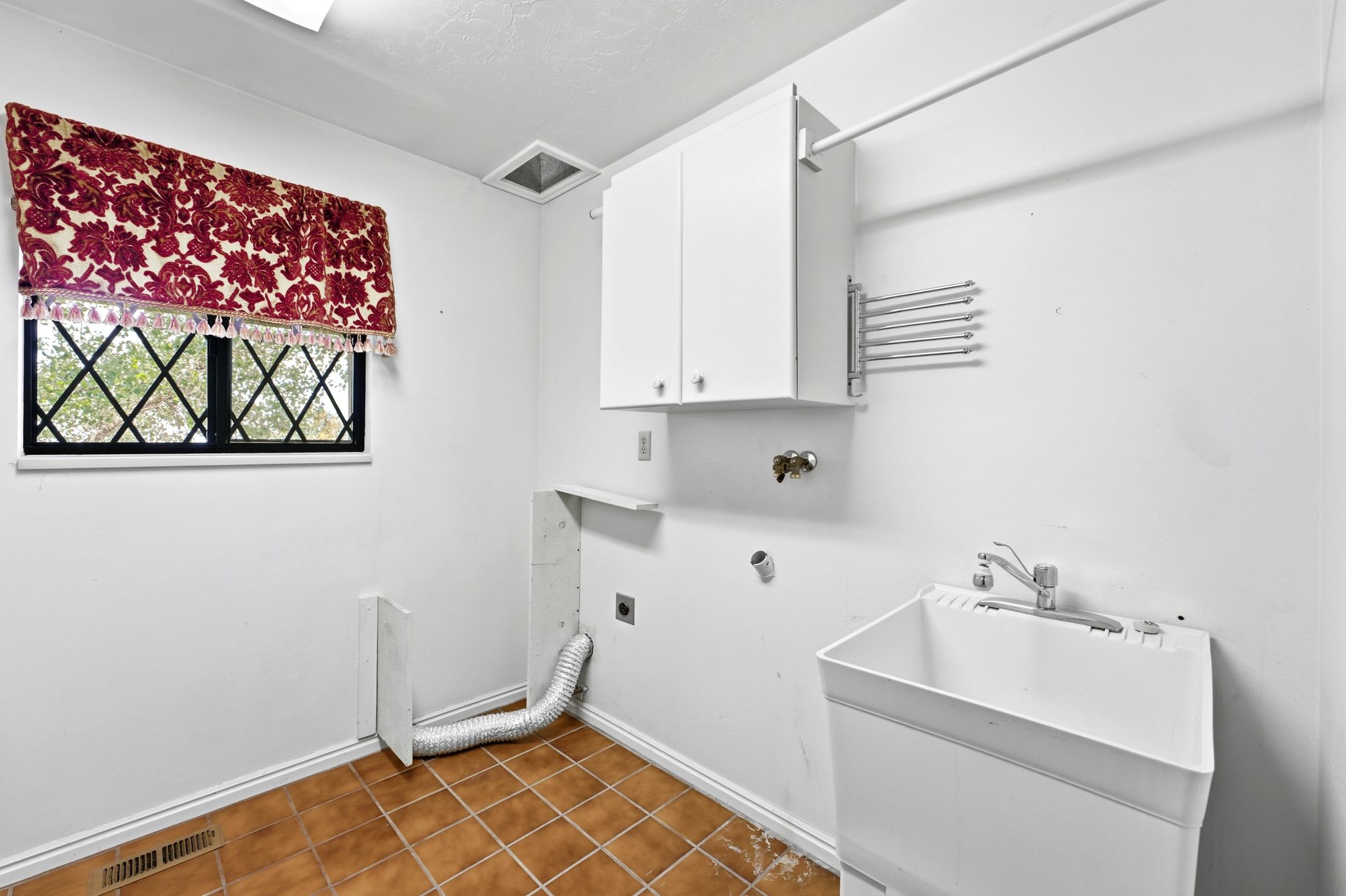 Utility room featuring a laundry basin with faucet, white wall-mounted cabinetry, an overhead clothing rod, and a folding drying rack