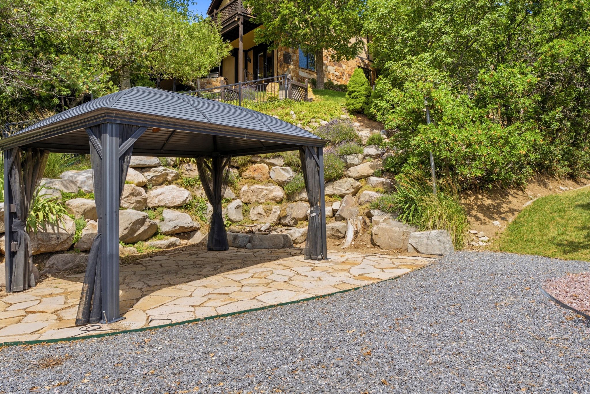Outdoor patio featuring a dark gray gazebo with privacy curtains, flagstone paving, and a gravel ground cover
