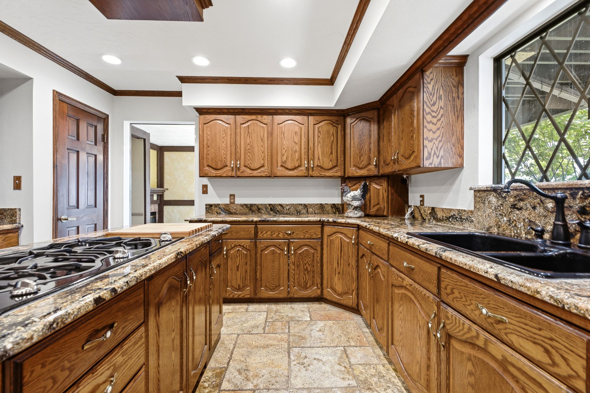 Kitchen featuring a built-in gas range, expansive wood cabinetry, stone countertops, a double basin sink with a dark faucet, and a window with a diamond pane design