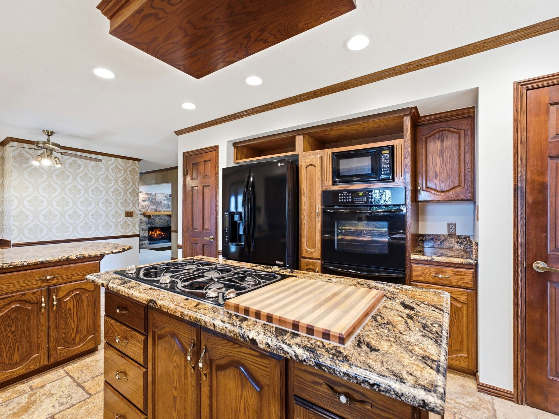 Kitchen featuring a gas cooktop on a central island, granite countertops,  integrated black appliances including a refrigerator, microwave, and double oven.