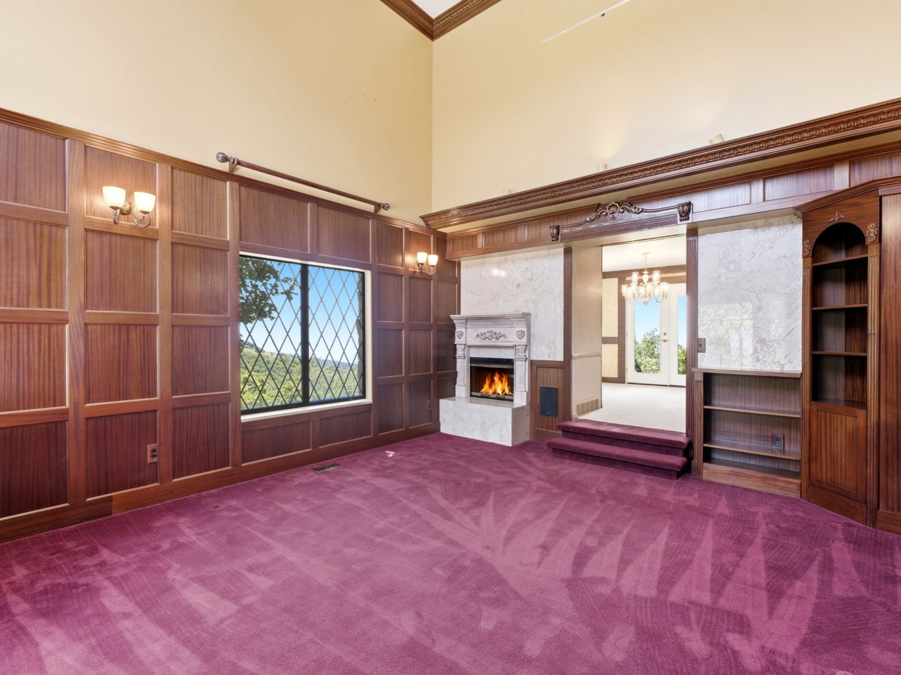 Living room featuring high ceilings, custom wood paneling with built-in shelves and cozy fireplace