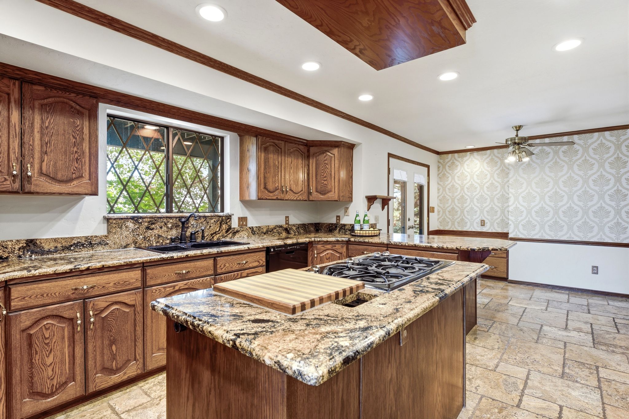 Spacious kitchen featuring wood cabinetry, granite countertops, a central island with a built-in cooktop, and recessed lighting