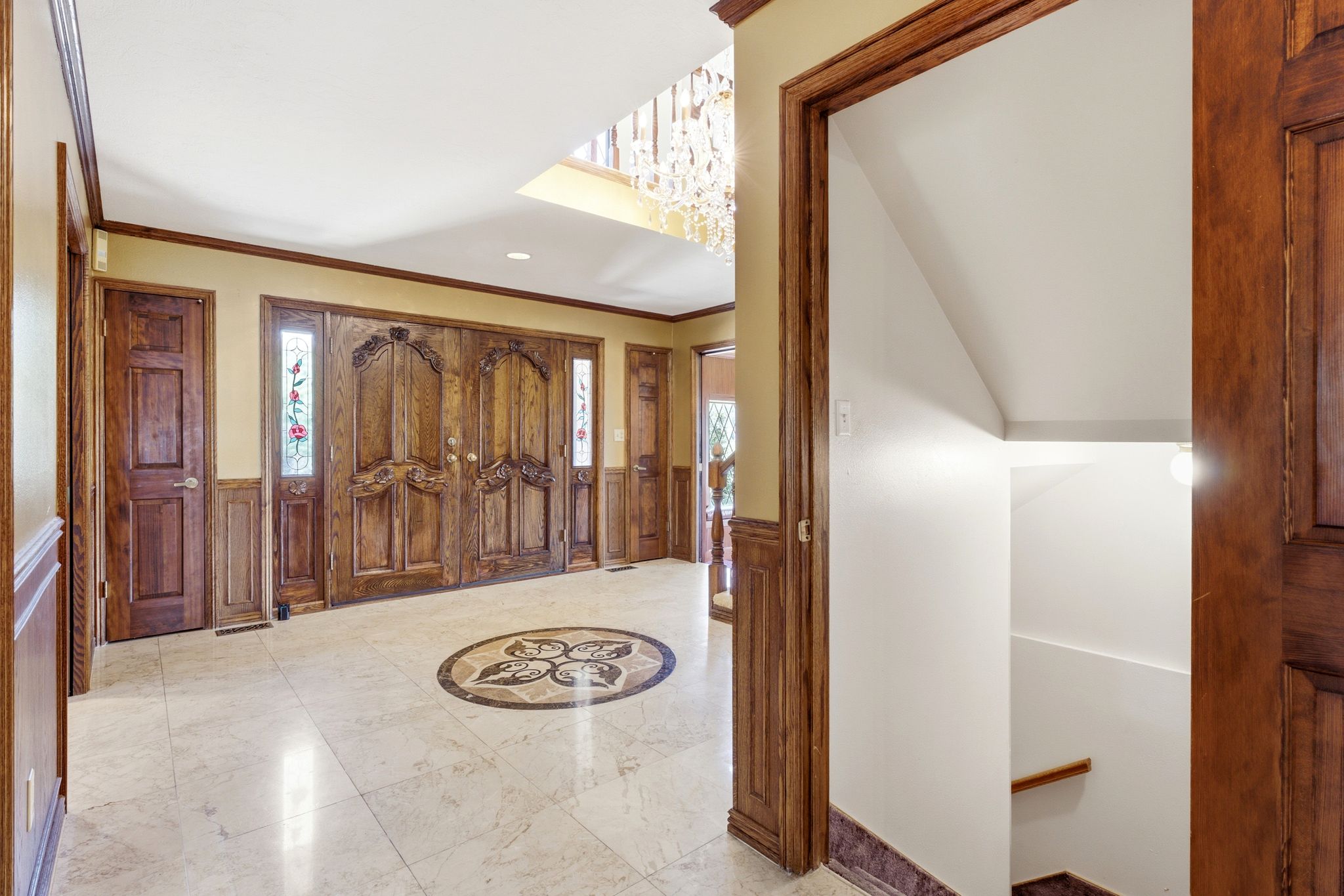 Grand entryway featuring ornate double doors with decorative carvings, marble tile flooring with a central medallion inlay.